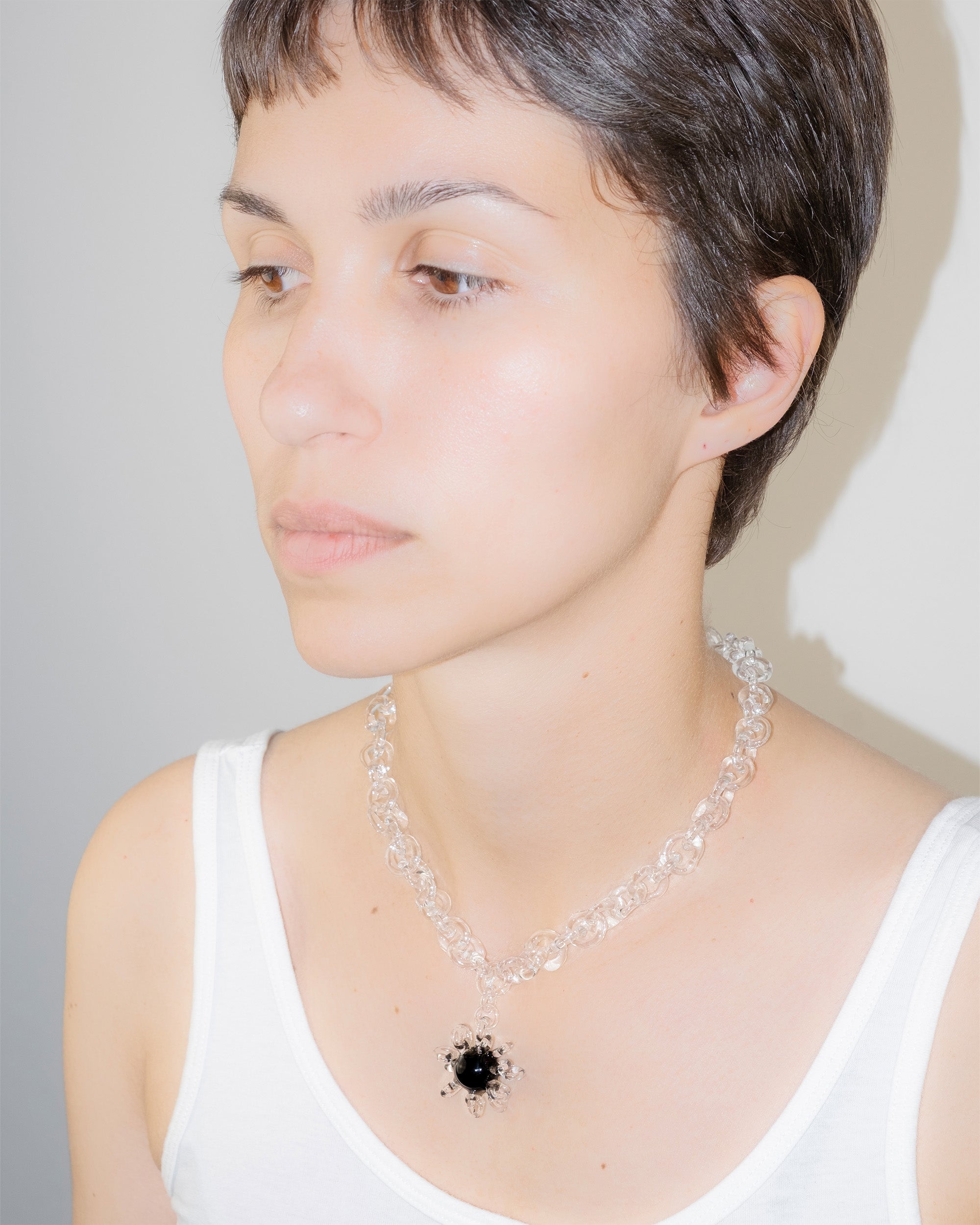 Model wearing bold glass chain necklace with black glass amulet centerpiece surrounded by transparent loops, handmade borosilicate jewelry.
