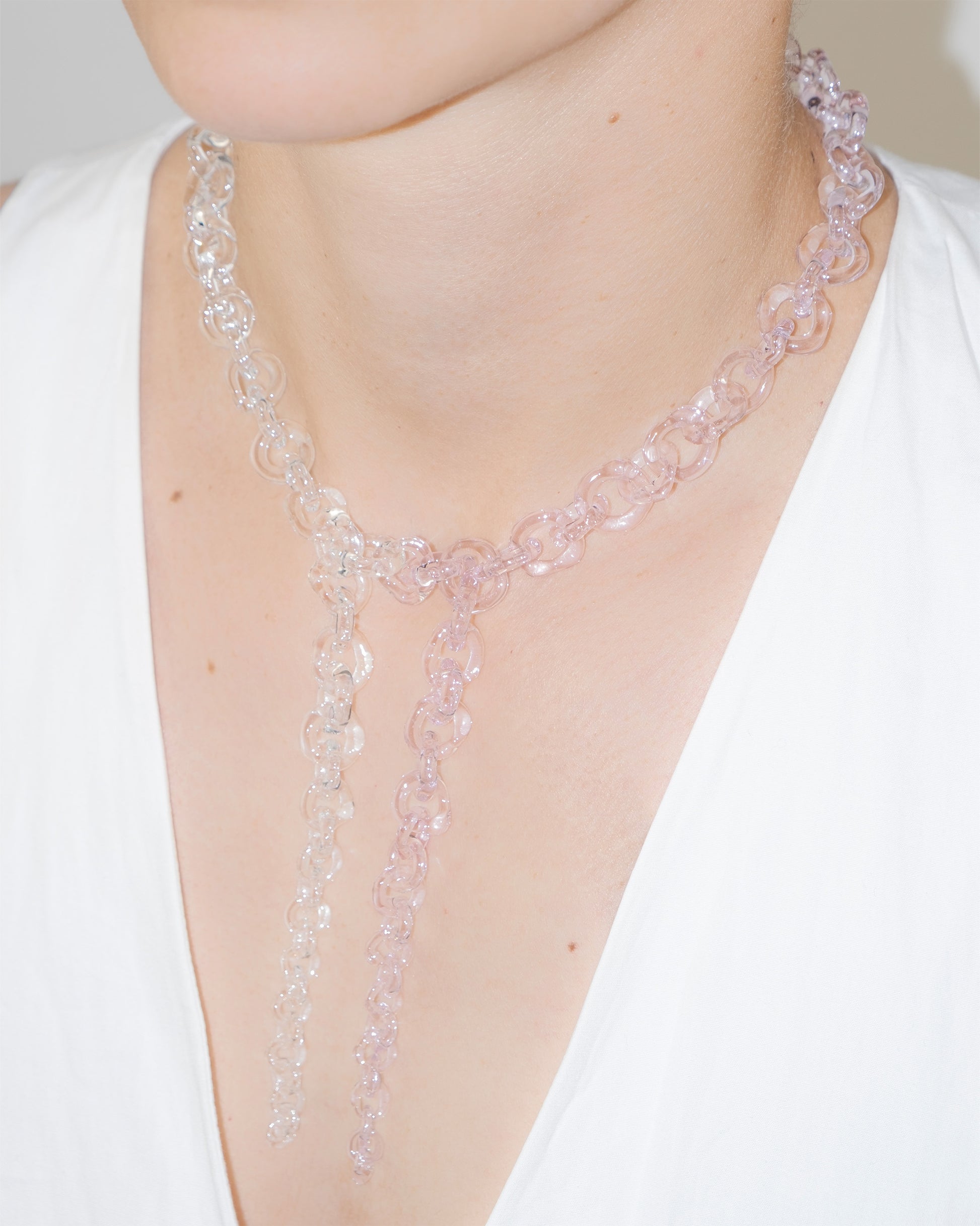 Model wearing bold transparent and pink glass chain necklace with two drop details, handmade borosilicate links and sterling silver clasp.