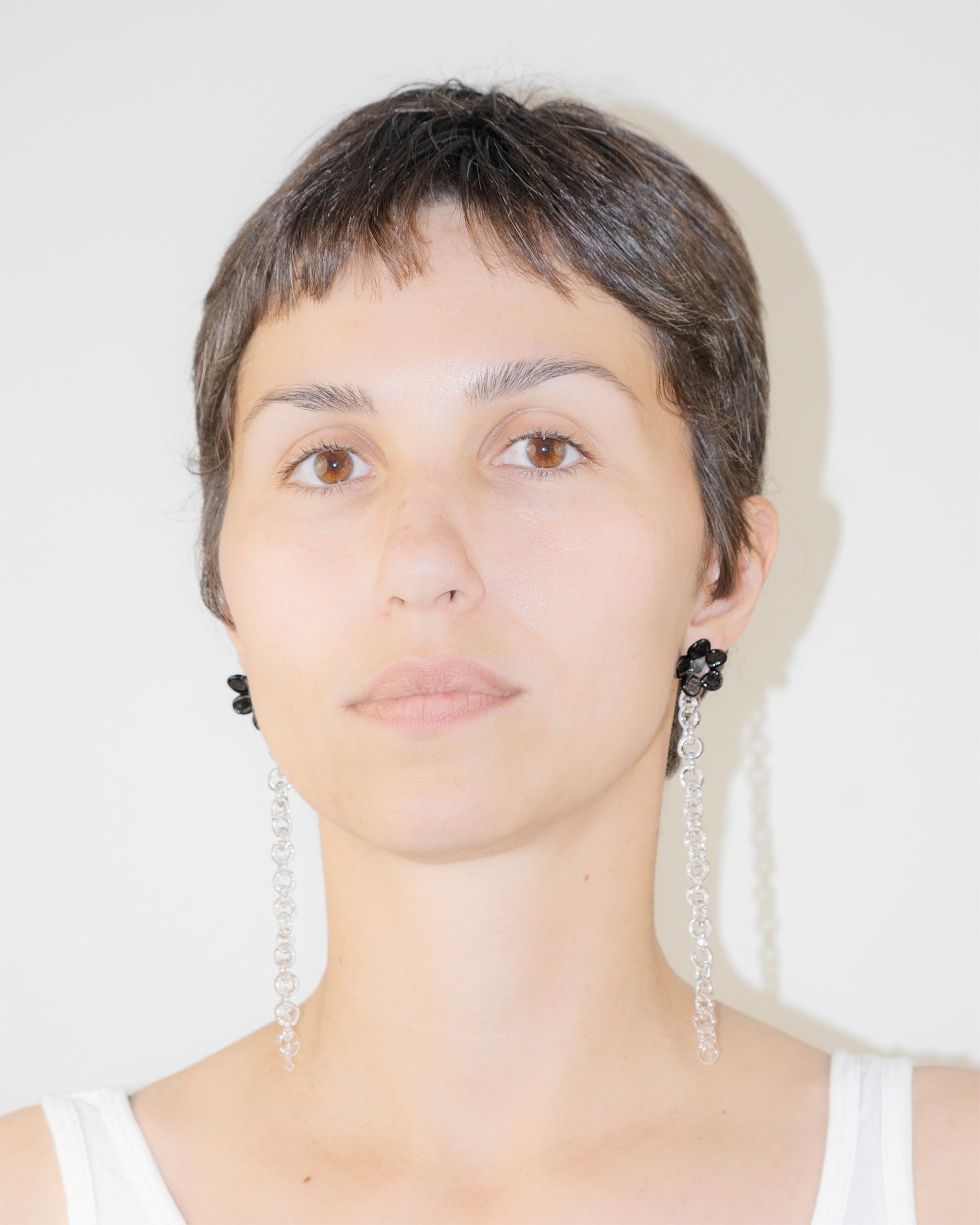 Model wearing Black Flowered Chain Earrings, handmade borosilicate glass flower with thin glass chain and silver studs.