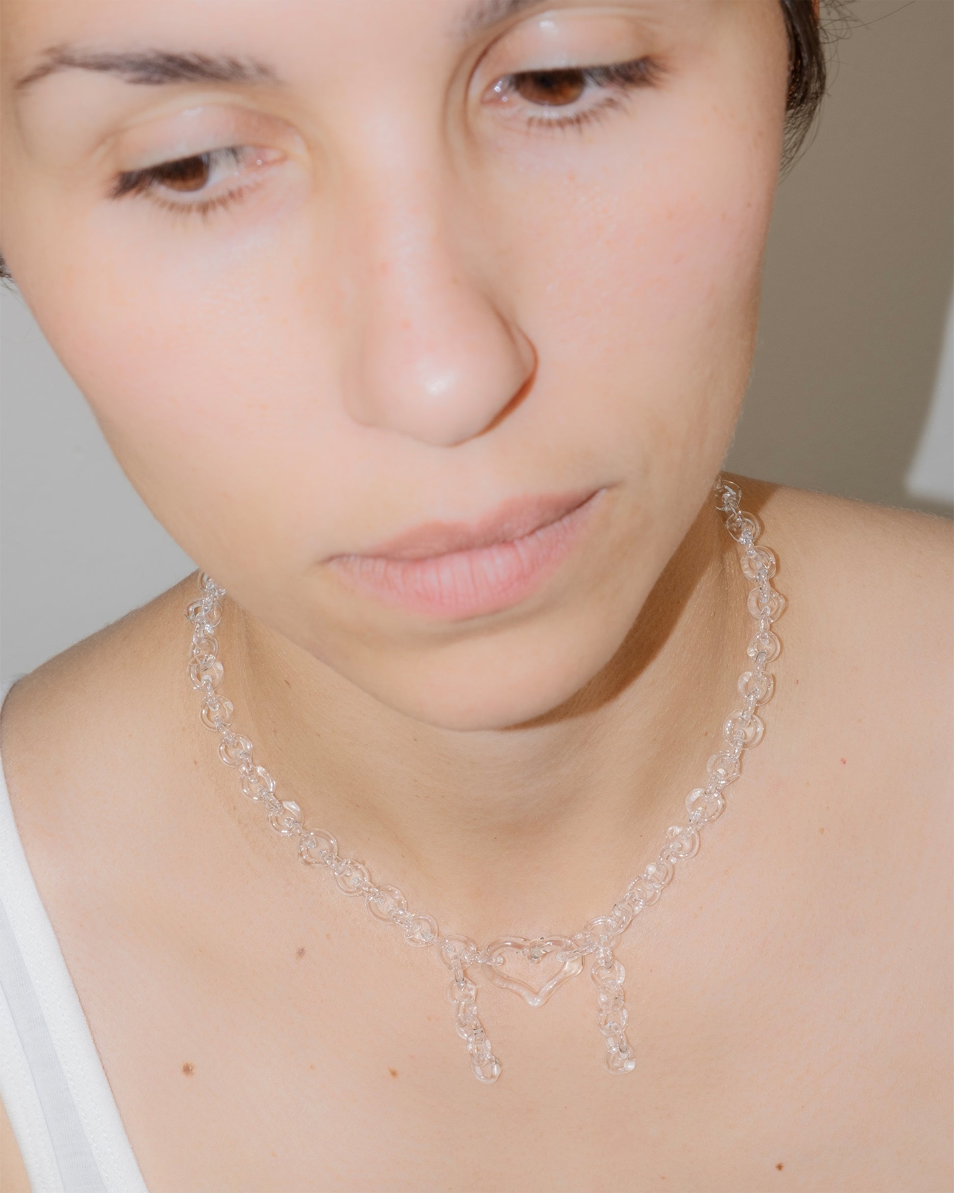 Model wearing transparent thin glass chain necklace with glass heart and two short side glass chains, handmade borosilicate jewelry.