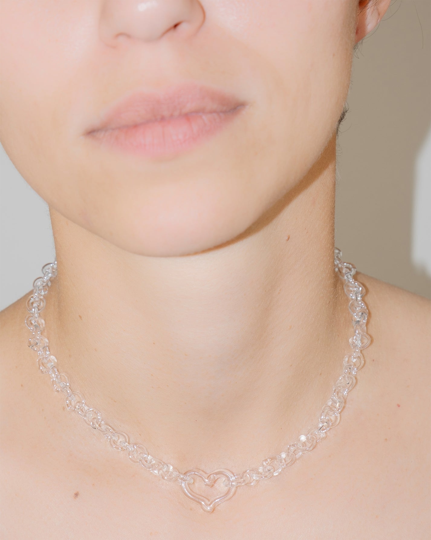 Model wearing transparent thin glass chain necklace with central glass heart, handmade borosilicate jewelry, adjustable fit.