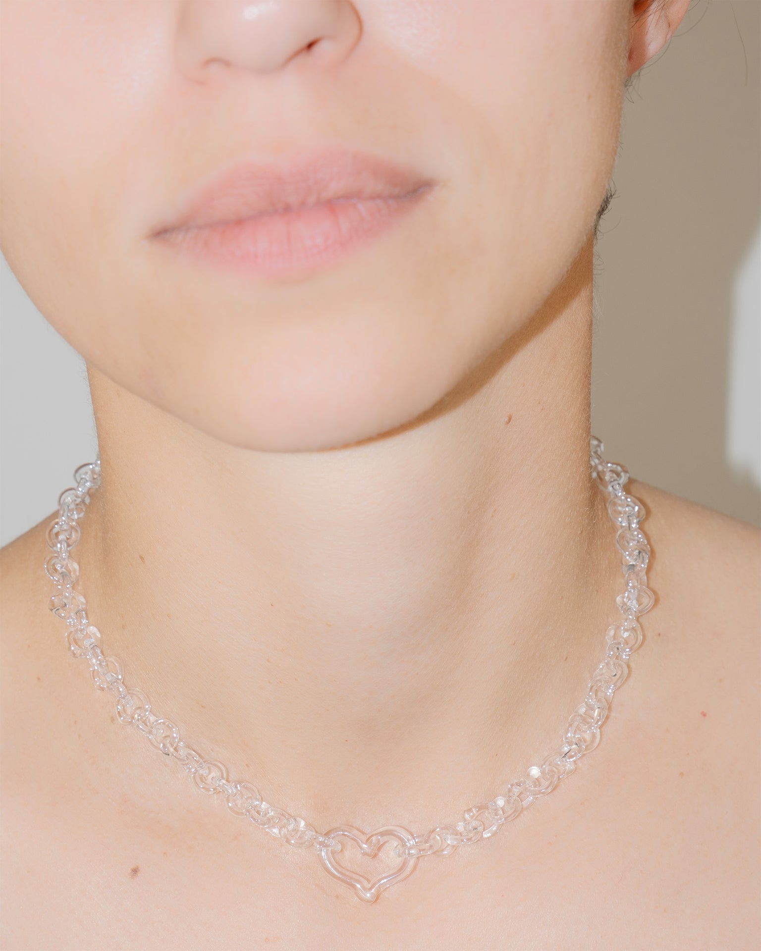 Model wearing transparent thin glass chain necklace with central glass heart, handmade borosilicate jewelry, adjustable fit.