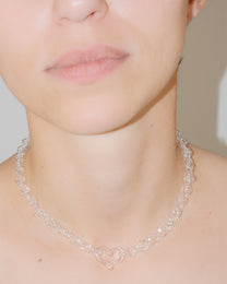 Model wearing transparent thin glass chain necklace with central glass heart, handmade borosilicate jewelry, adjustable fit.