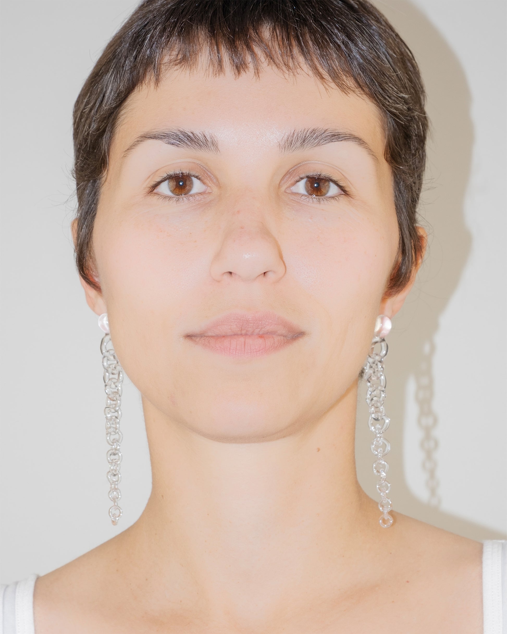 Model wearing Tapered Drop Earrings, handmade borosilicate glass tapering from thick to thin with orb-like top detail and sterling silver studs.