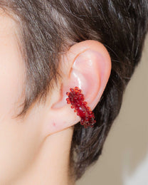 Detail view of red glass ear cuff, highlighting the pattern of dots and tiny spheres along the curve.