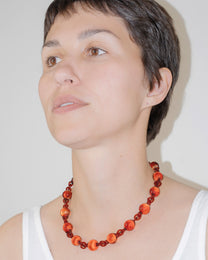 Model wearing red Orb Necklace with solid glass spheres linked into a continuous glass chain, handmade borosilicate jewelry.