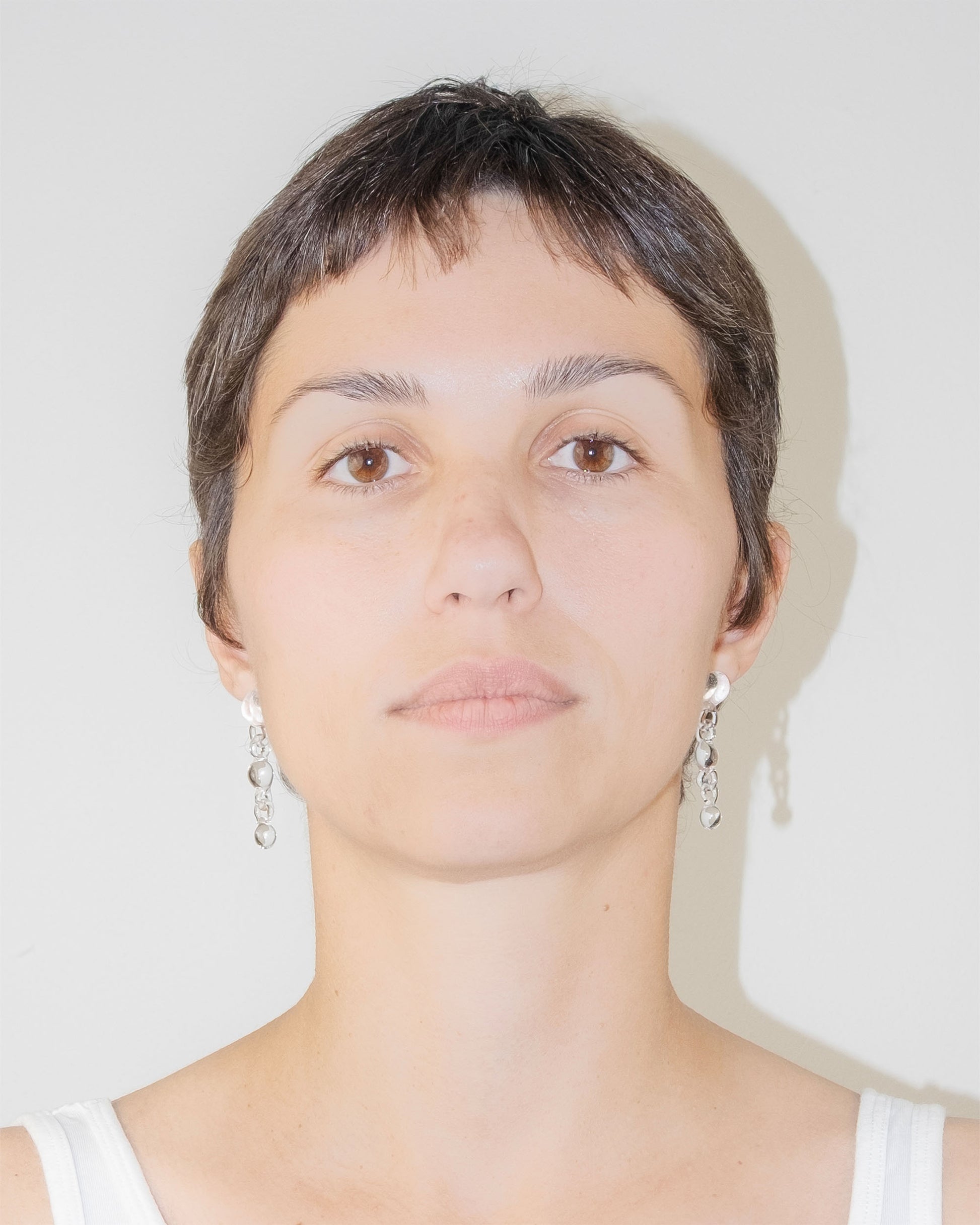 Model wearing Orb Earrings, handmade borosilicate glass design with three orbs in a vertical drop, mounted on sterling silver studs.