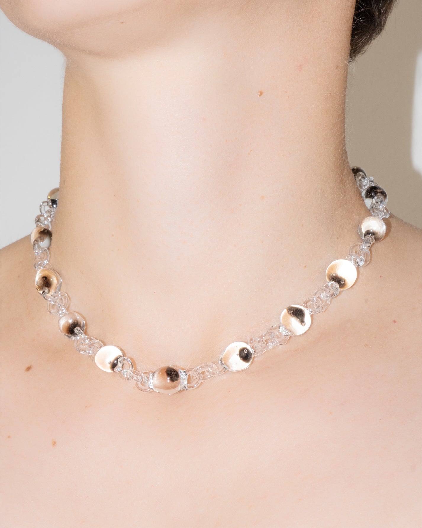 Model wearing Orb Mini Necklace with transparent glass spheres containing black-tinted fading accents, handmade borosilicate jewelry.