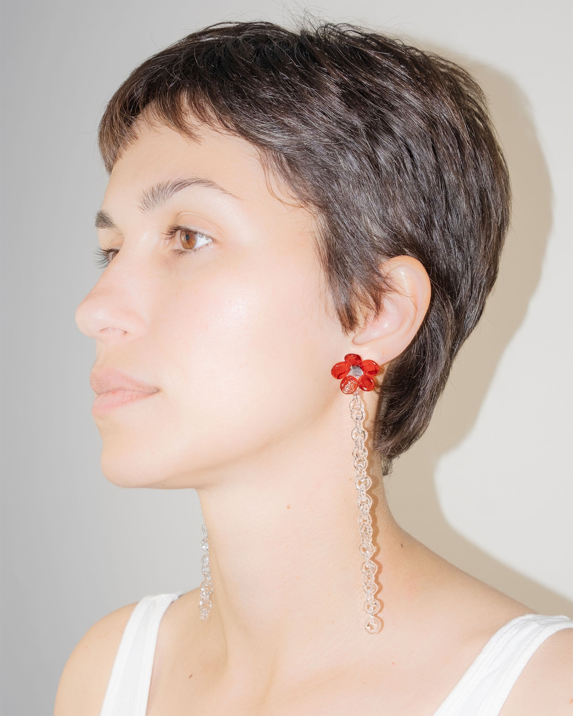 Model wearing Flowered Chain Earrings in red borosilicate glass with transparent center and thin glass chain.