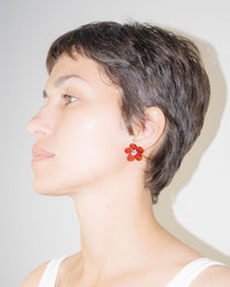 Model wearing Flower Stud Earrings in borosilicate glass with red petals and transparent center, sterling silver studs.