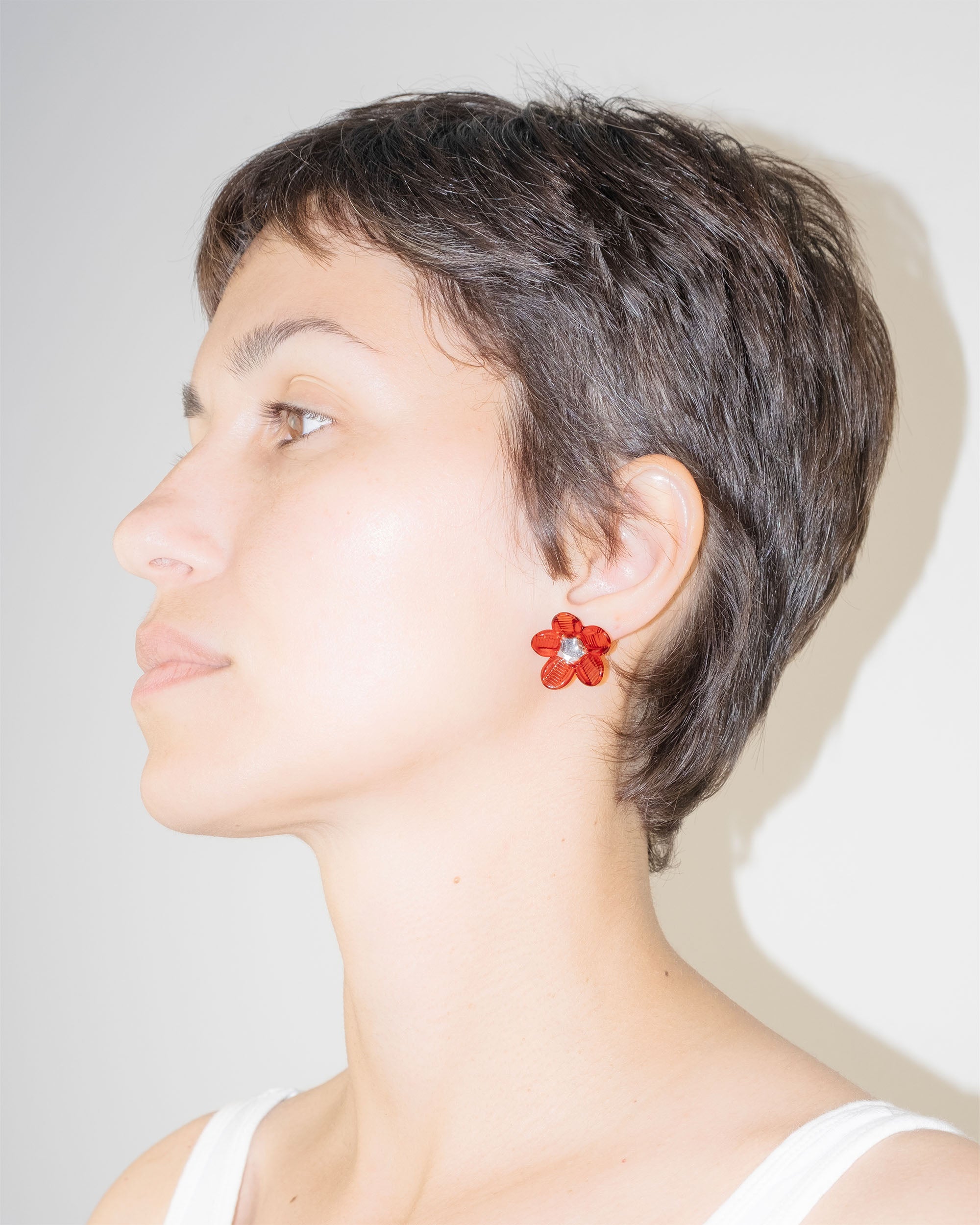 Model wearing Flower Stud Earrings in borosilicate glass with red petals and transparent center, sterling silver studs.