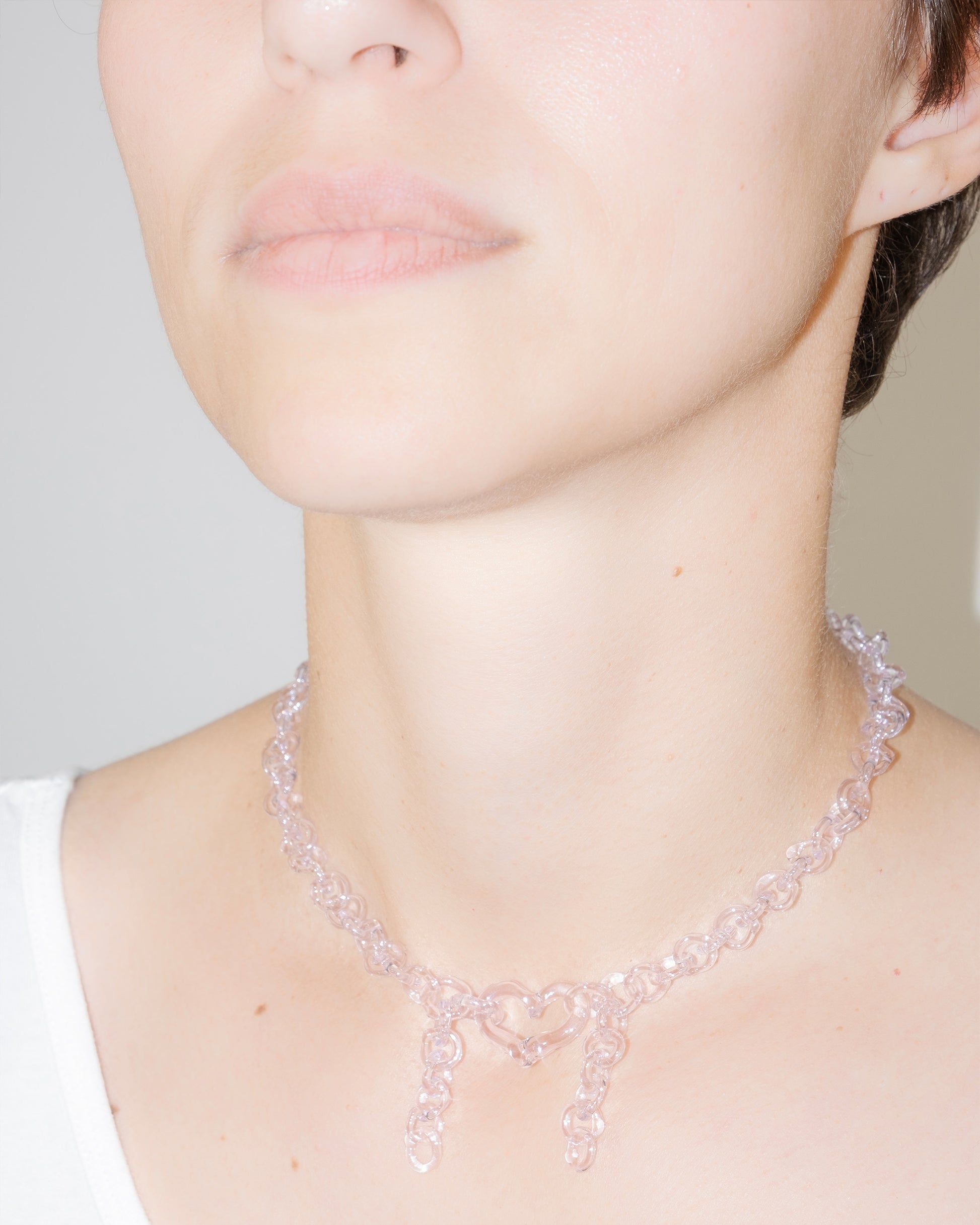 Model wearing pink thin glass chain necklace with central heart and two short side glass chains, handmade borosilicate jewelry.