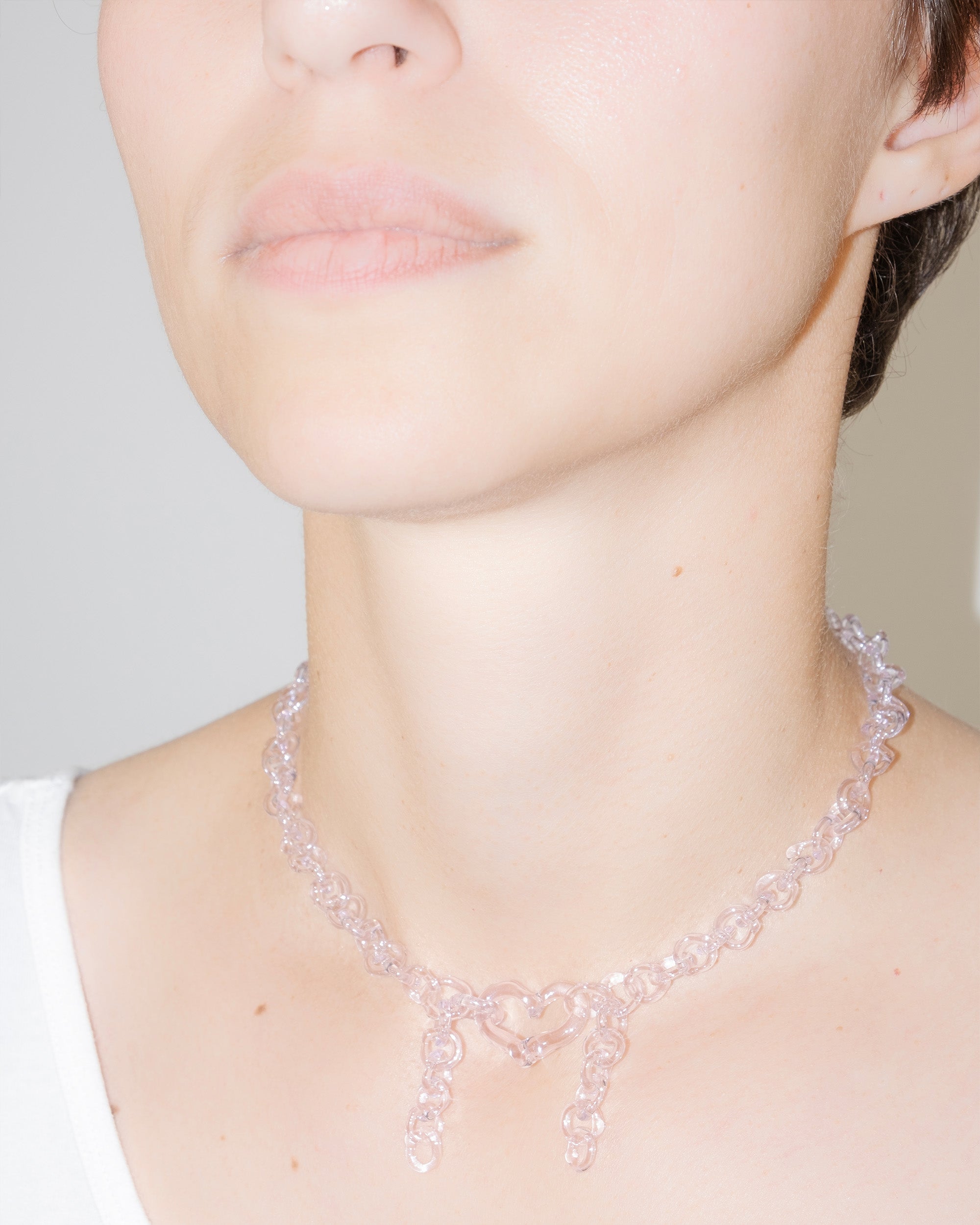 Model wearing pink thin glass chain necklace with central heart and two short side glass chains, handmade borosilicate jewelry.