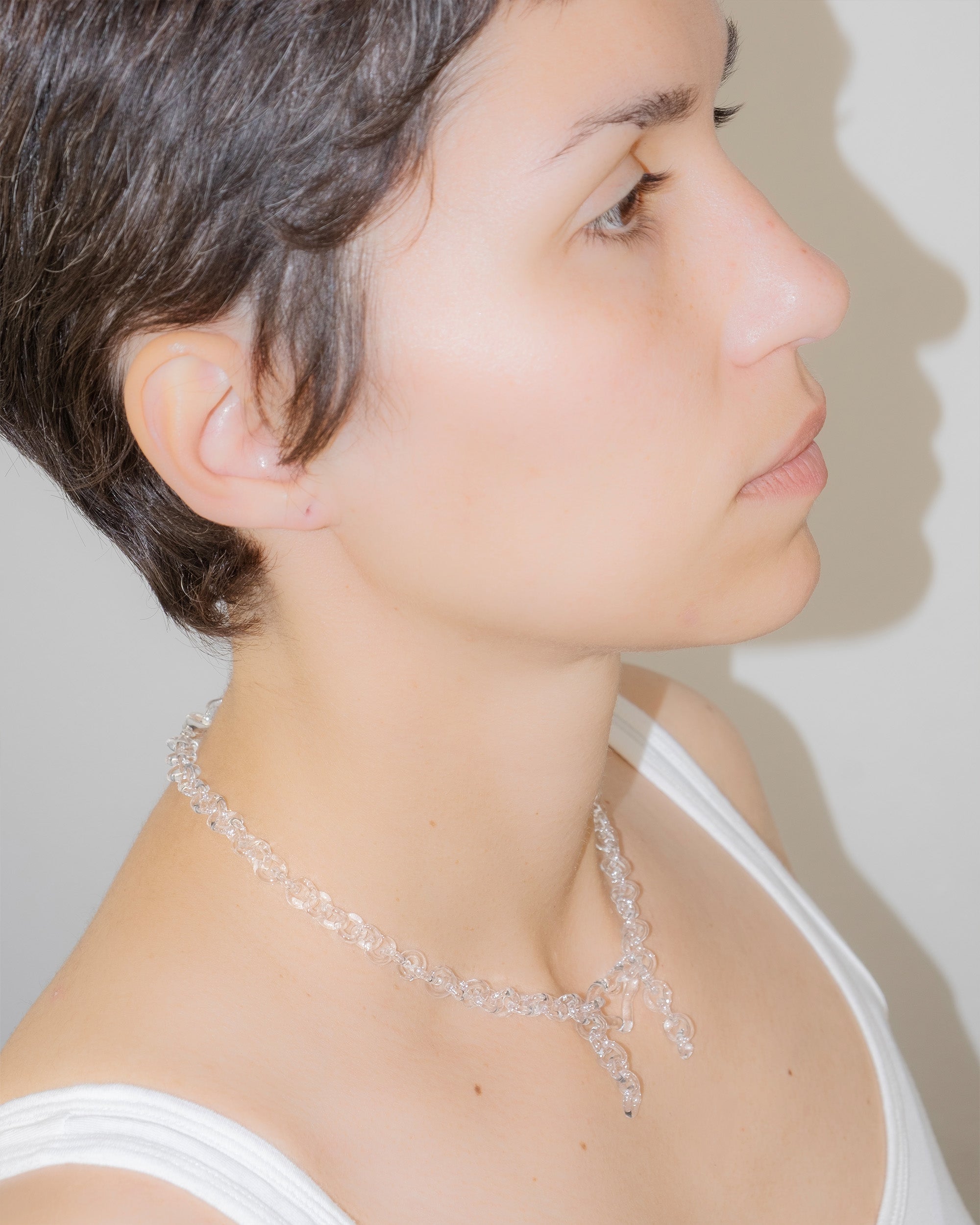 Model wearing transparent thin glass chain necklace with glass heart and two short side glass chains, handmade borosilicate jewelry.