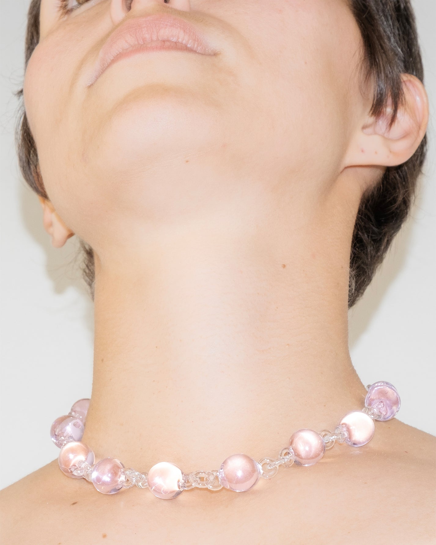 Model wearing pink Orb Necklace with transparent glass links connecting solid glass spheres, handmade borosilicate jewelry.
