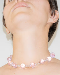 Model wearing pink Orb Necklace with transparent glass links connecting solid glass spheres, handmade borosilicate jewelry.