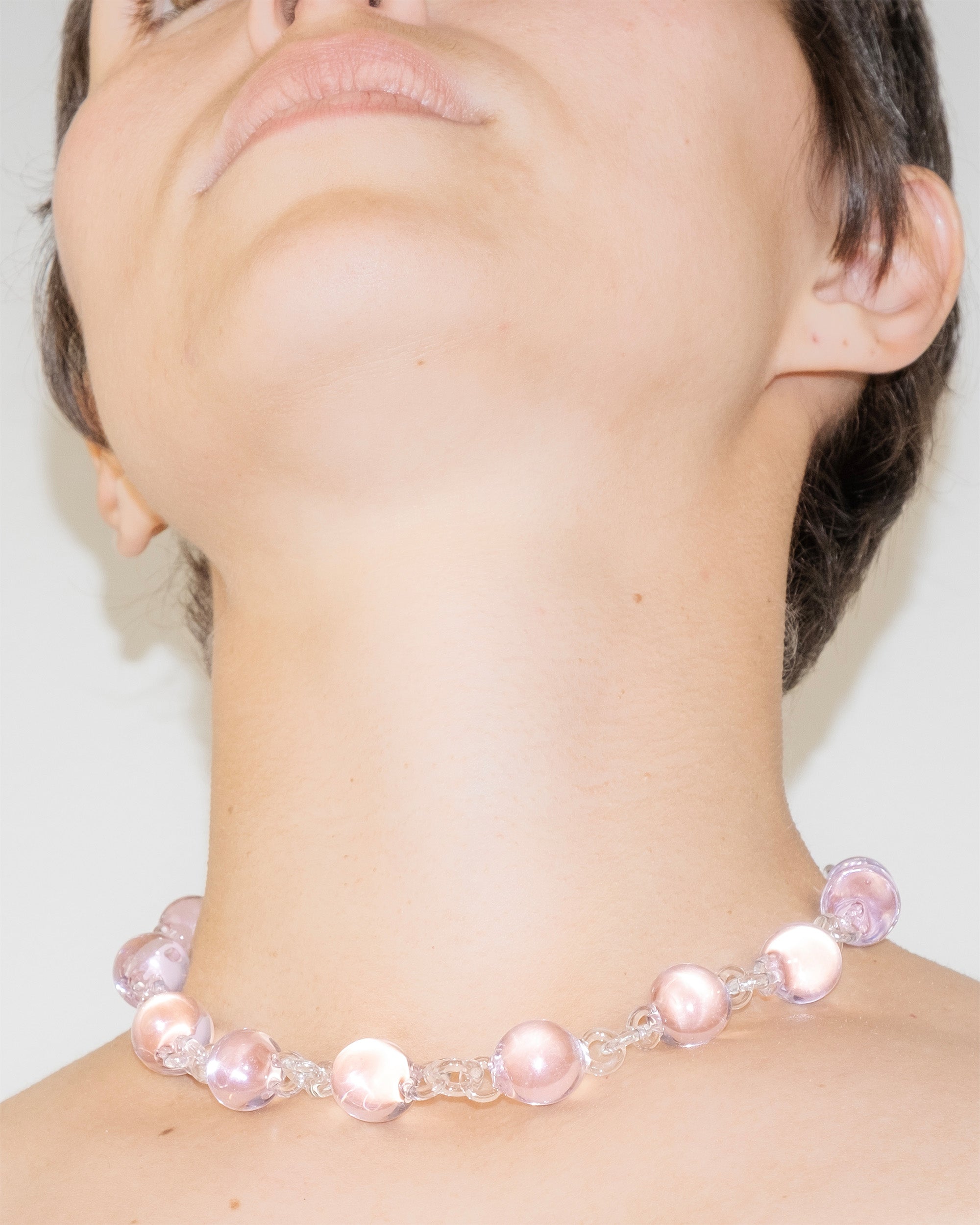 Model wearing pink Orb Necklace with transparent glass links connecting solid glass spheres, handmade borosilicate jewelry.