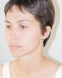 Model wearing Orb Earrings, handmade borosilicate glass design with three orbs in a vertical drop, mounted on sterling silver studs.