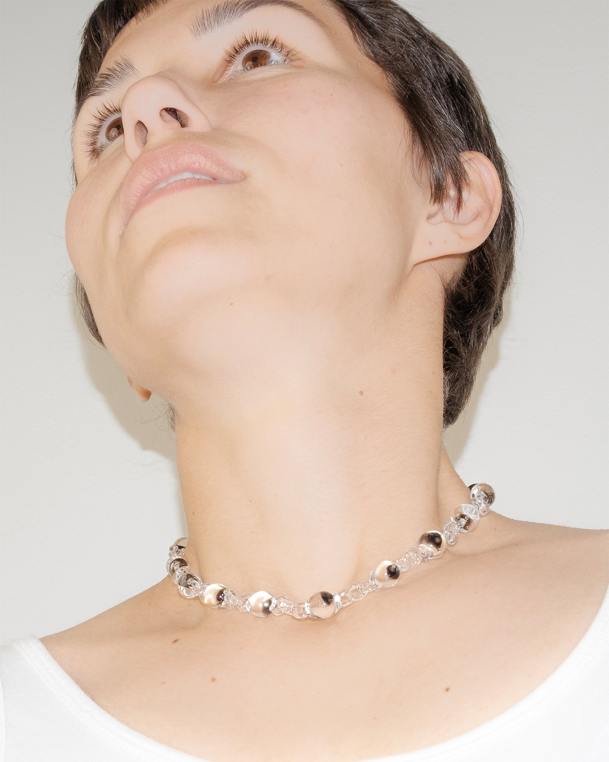 Model wearing Orb Mini Necklace with transparent glass spheres containing black-tinted fading accents, handmade borosilicate jewelry.
