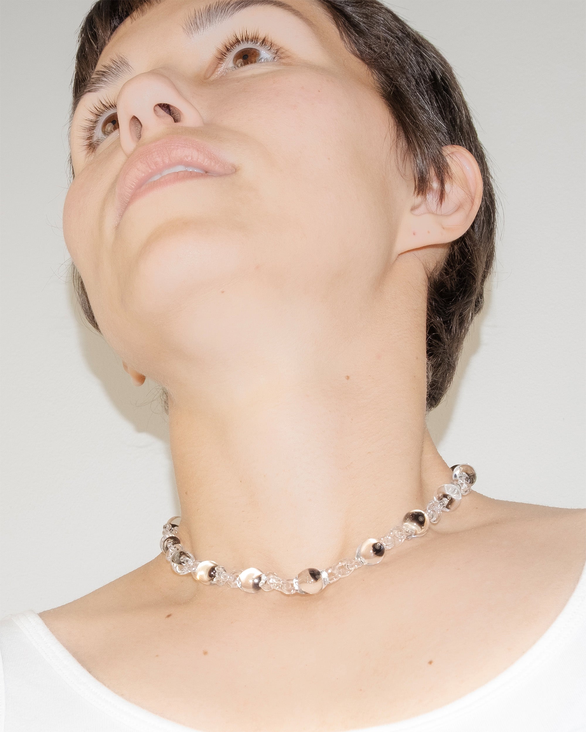Model wearing Orb Mini Necklace with transparent glass spheres containing black-tinted fading accents, handmade borosilicate jewelry.