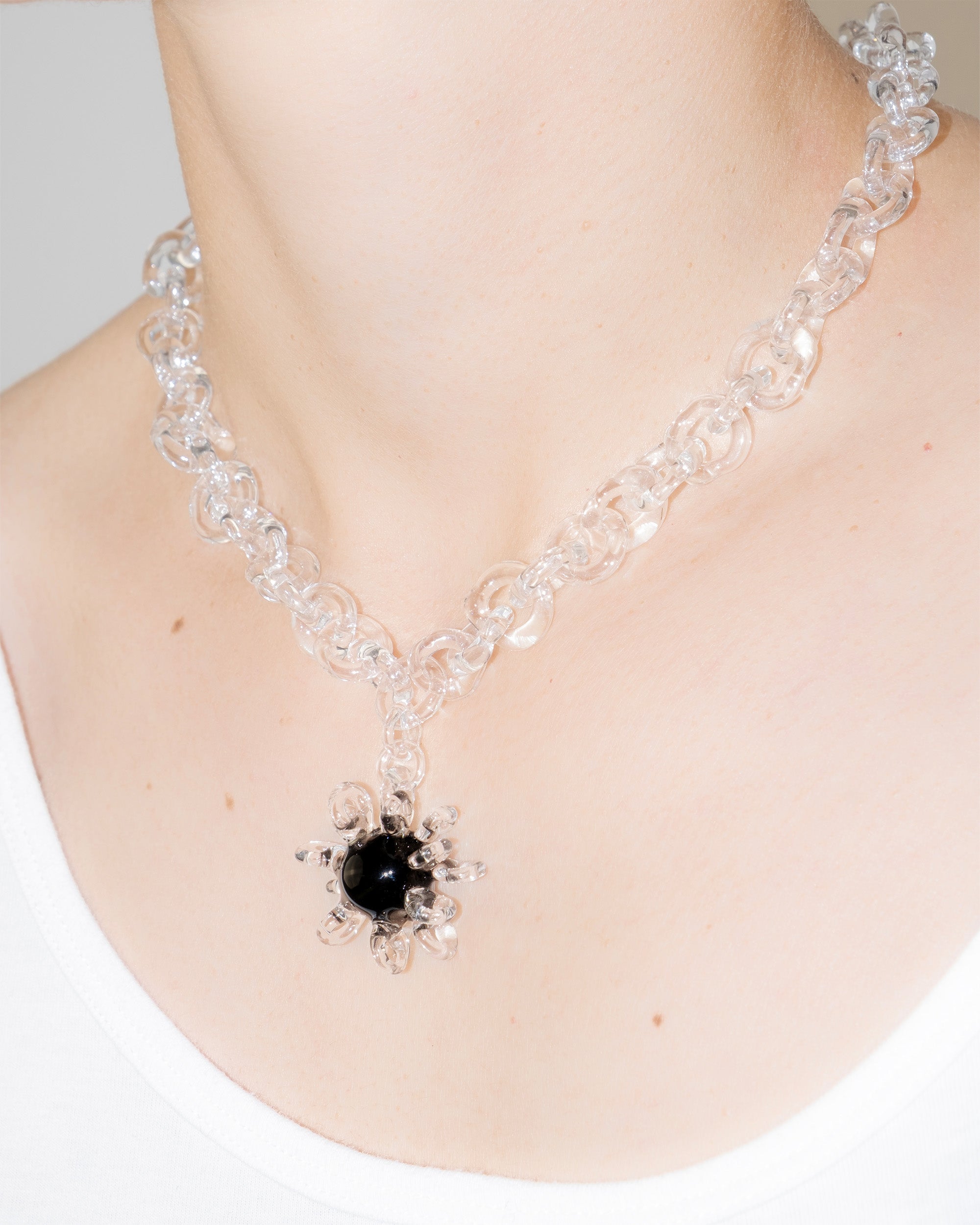 Model wearing bold glass chain necklace with black glass amulet centerpiece surrounded by transparent loops, handmade borosilicate jewelry.