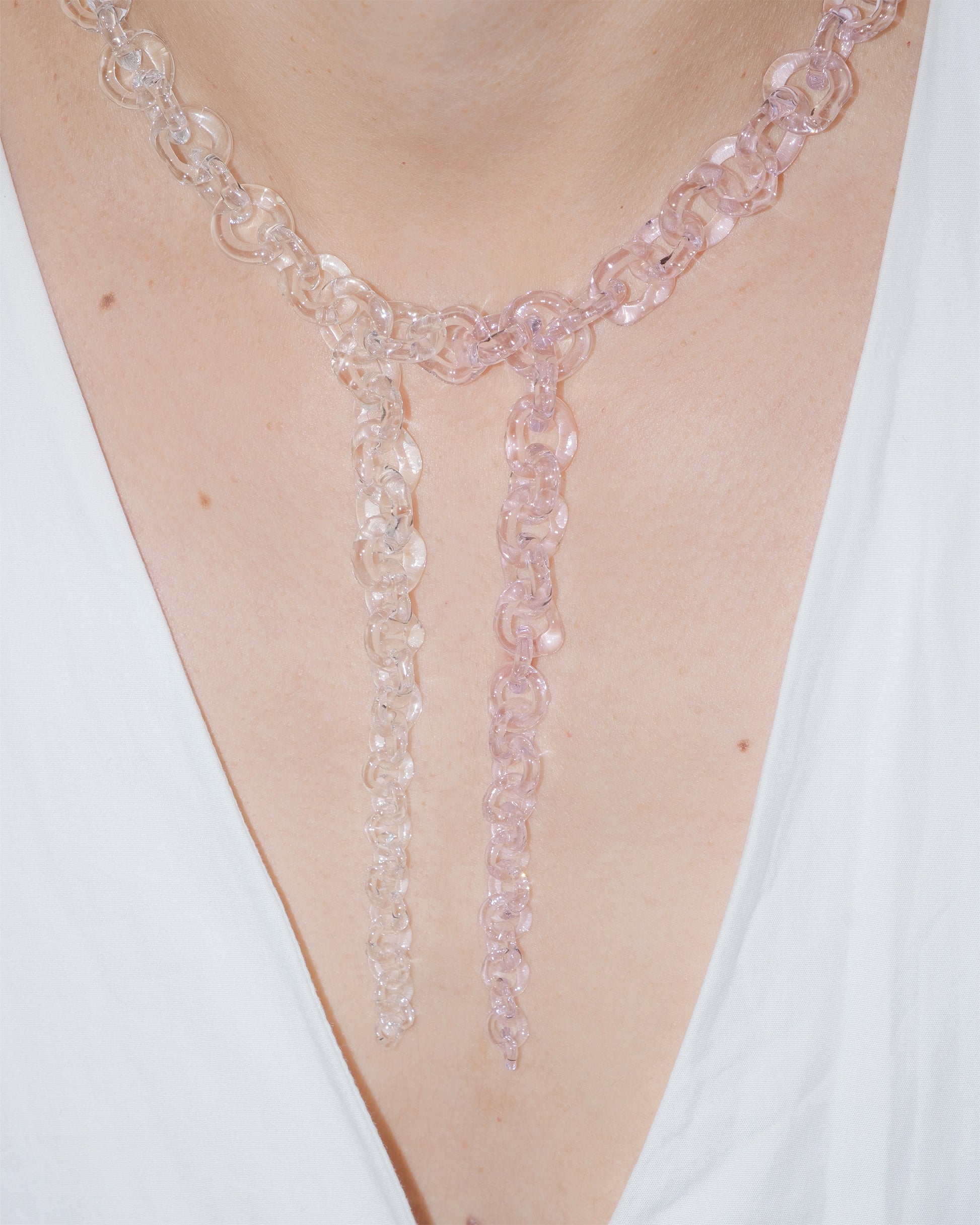 Model wearing bold transparent and pink glass chain necklace with two drop details, handmade borosilicate links and sterling silver clasp.