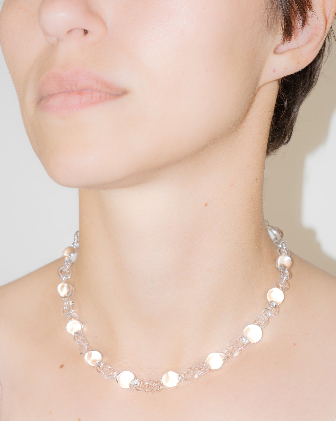 Model wearing transparent Orb Mini Necklace, handmade from smaller solid borosilicate glass spheres in a continuous chain.