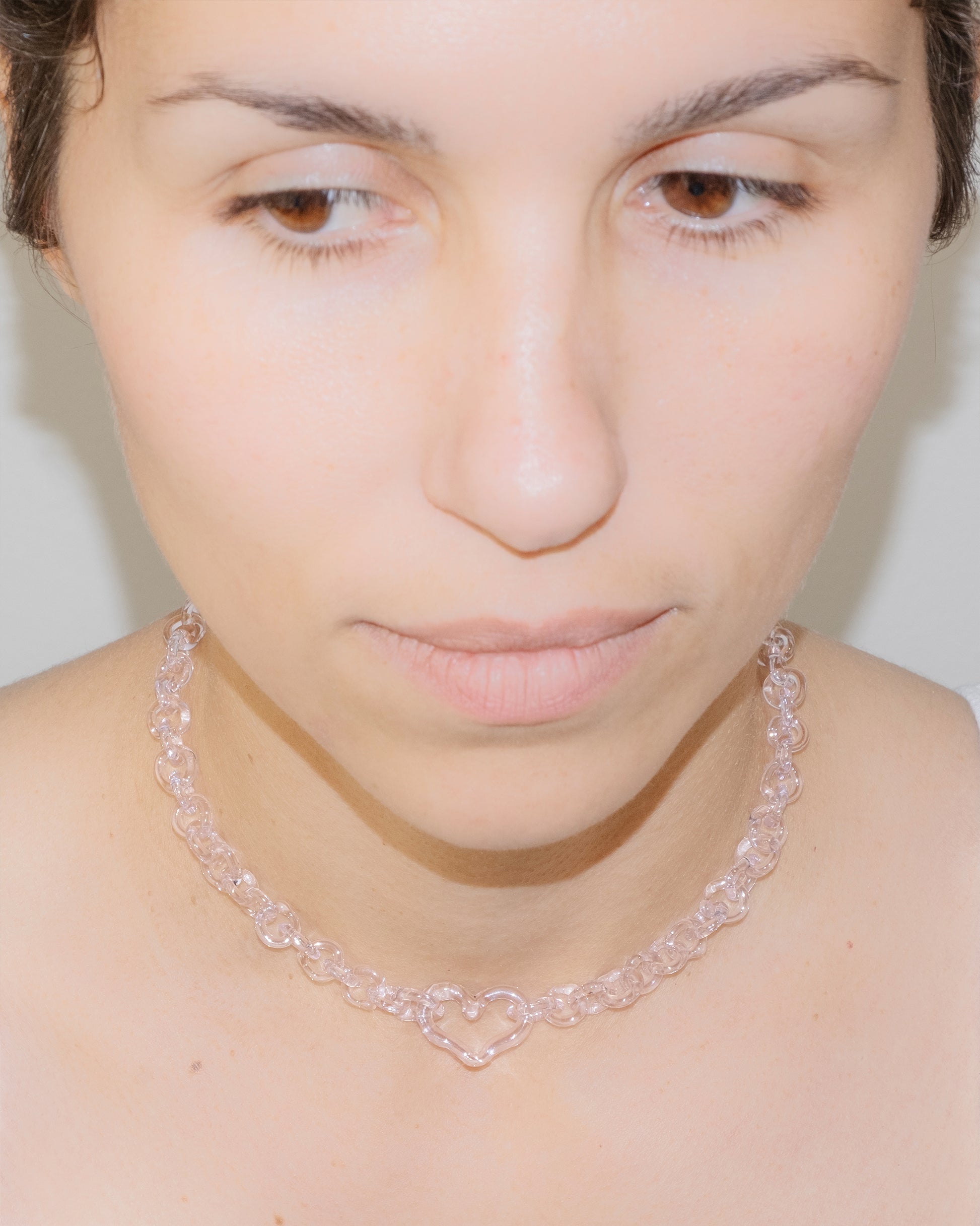Model wearing pink thin glass chain necklace with central glass heart, handmade borosilicate jewelry, adjustable design.