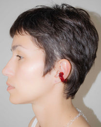 Side profile of a person with short dark hair wearing a red ear cuff against a neutral background