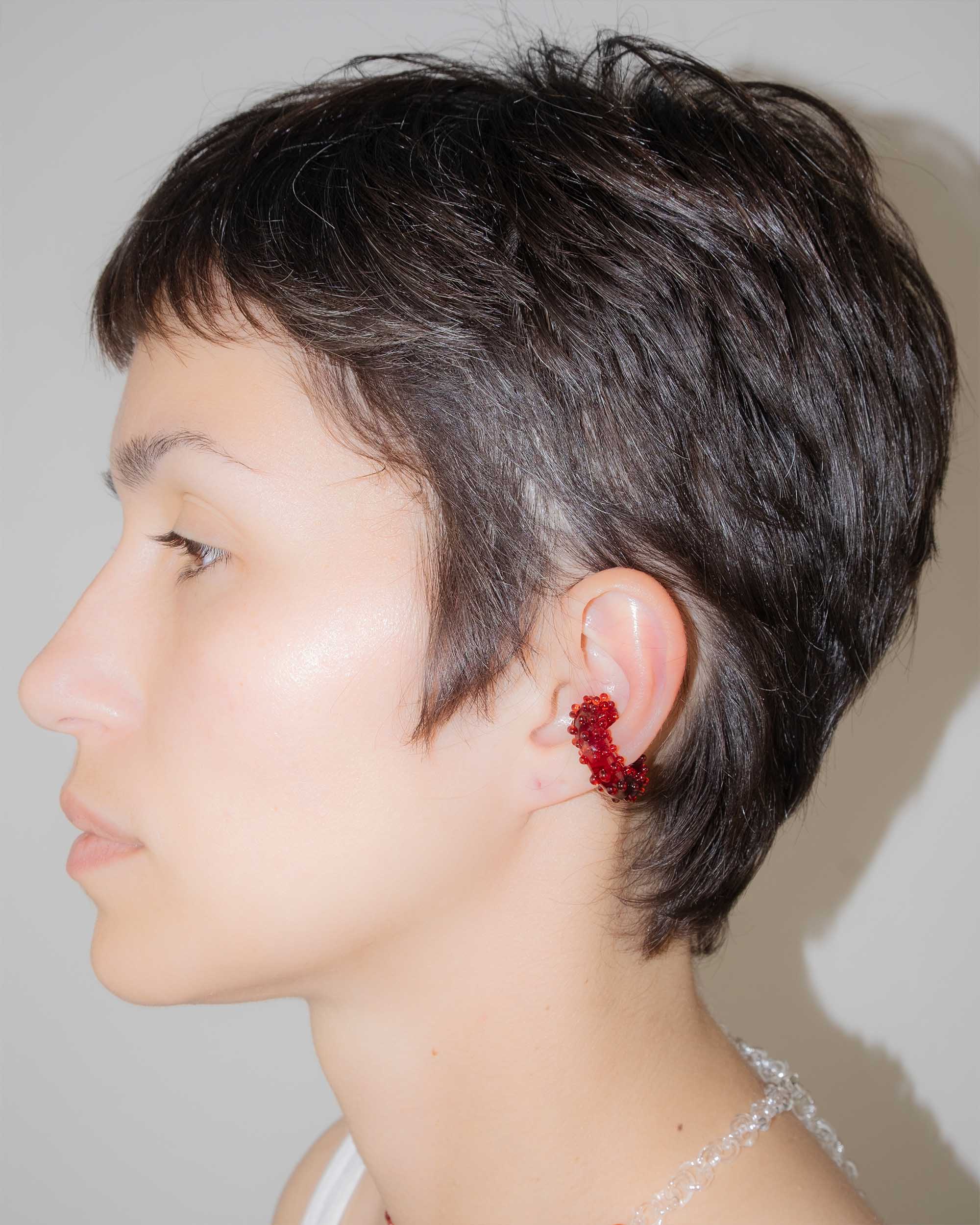 Side profile of a person with short dark hair wearing a red ear cuff against a neutral background