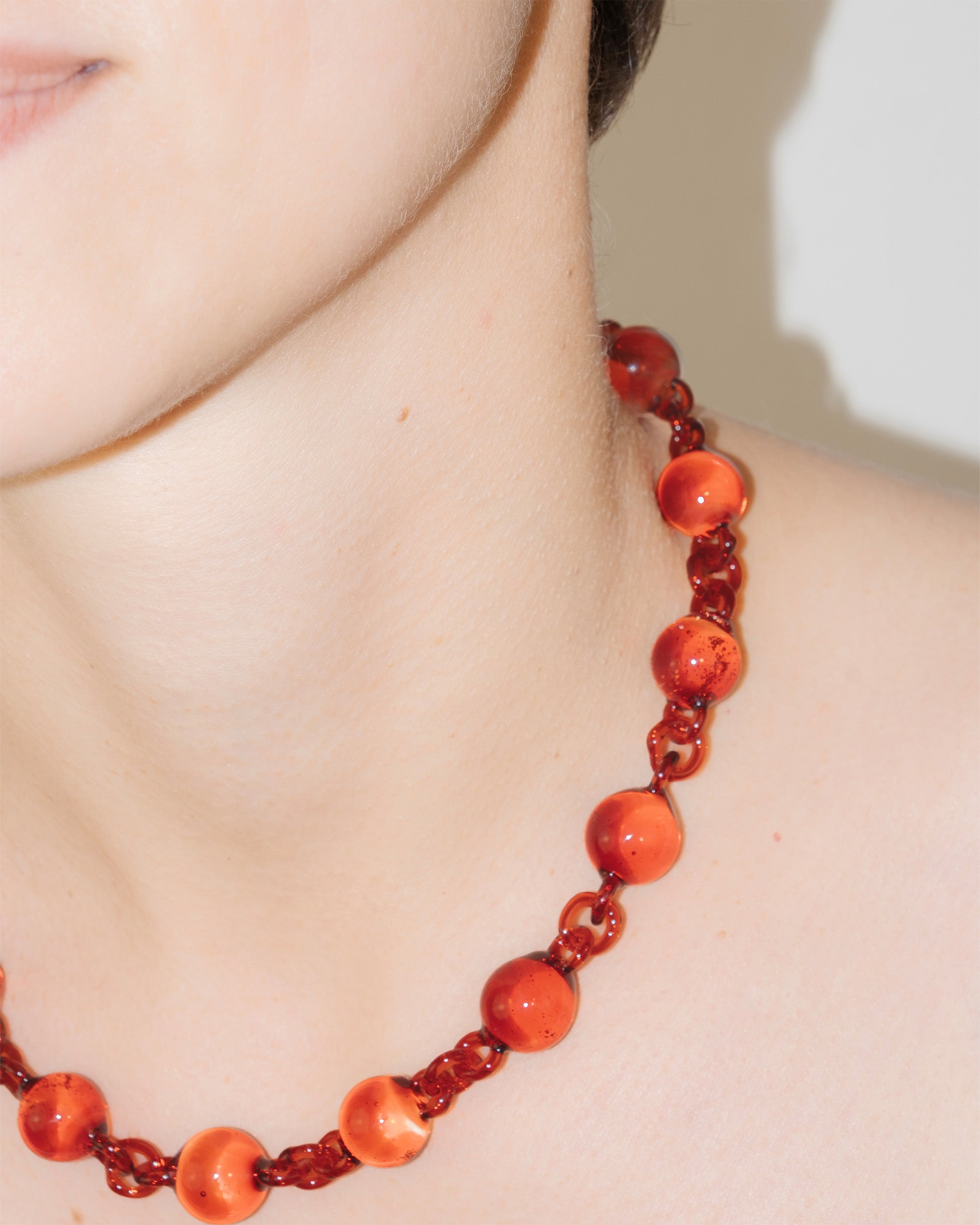 Model wearing red Orb Necklace with solid glass spheres linked into a continuous glass chain, handmade borosilicate jewelry.