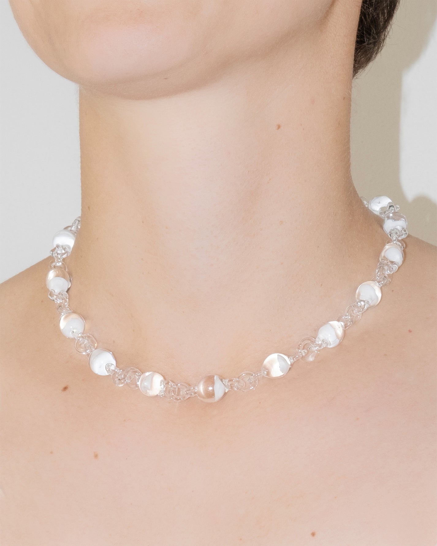 Close-up of Orb Mini Necklace showing transparent glass spheres with subtle white tint fading inside, handmade borosilicate glass piece.