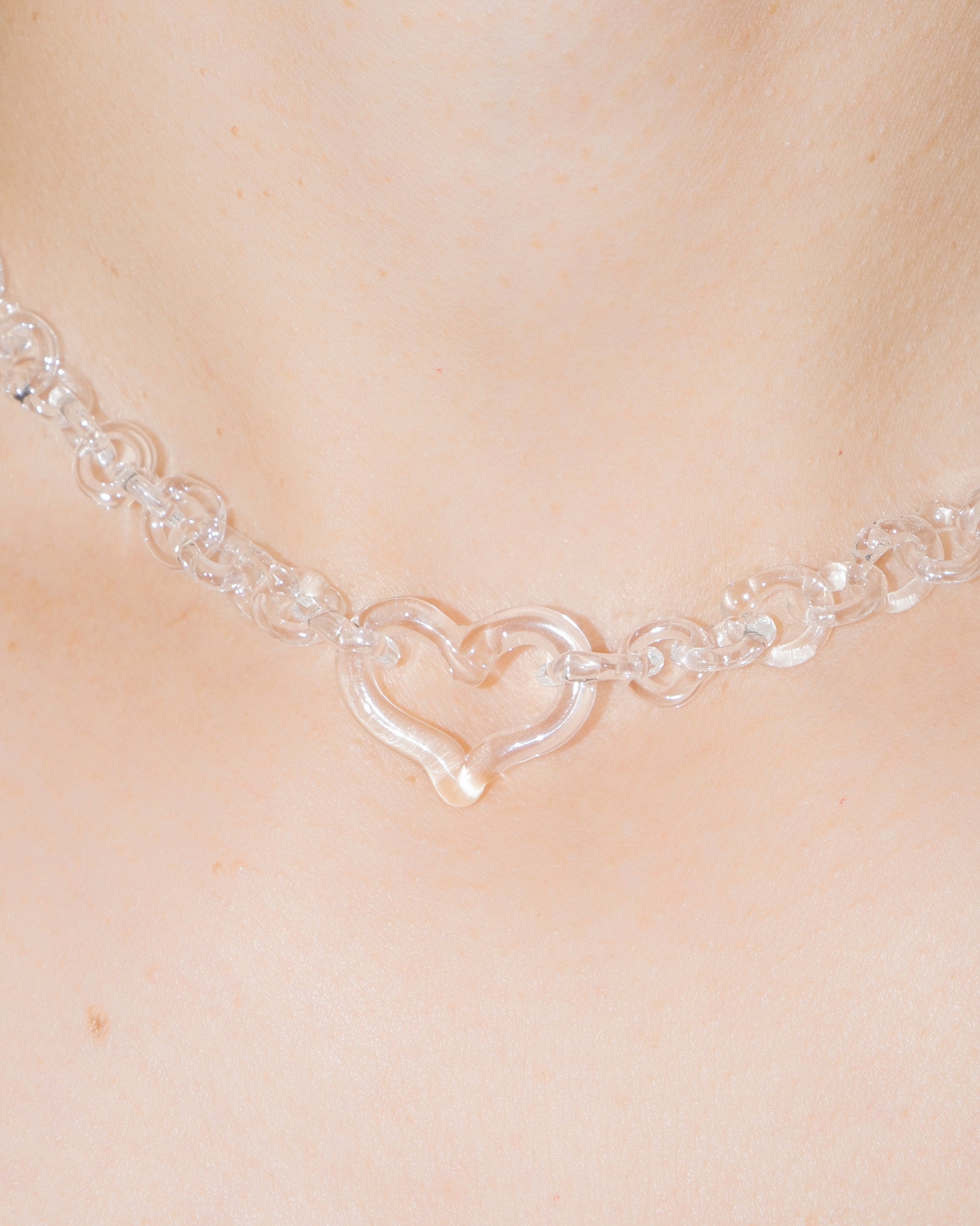 Model wearing transparent thin glass chain necklace with central glass heart, handmade borosilicate jewelry, adjustable fit.