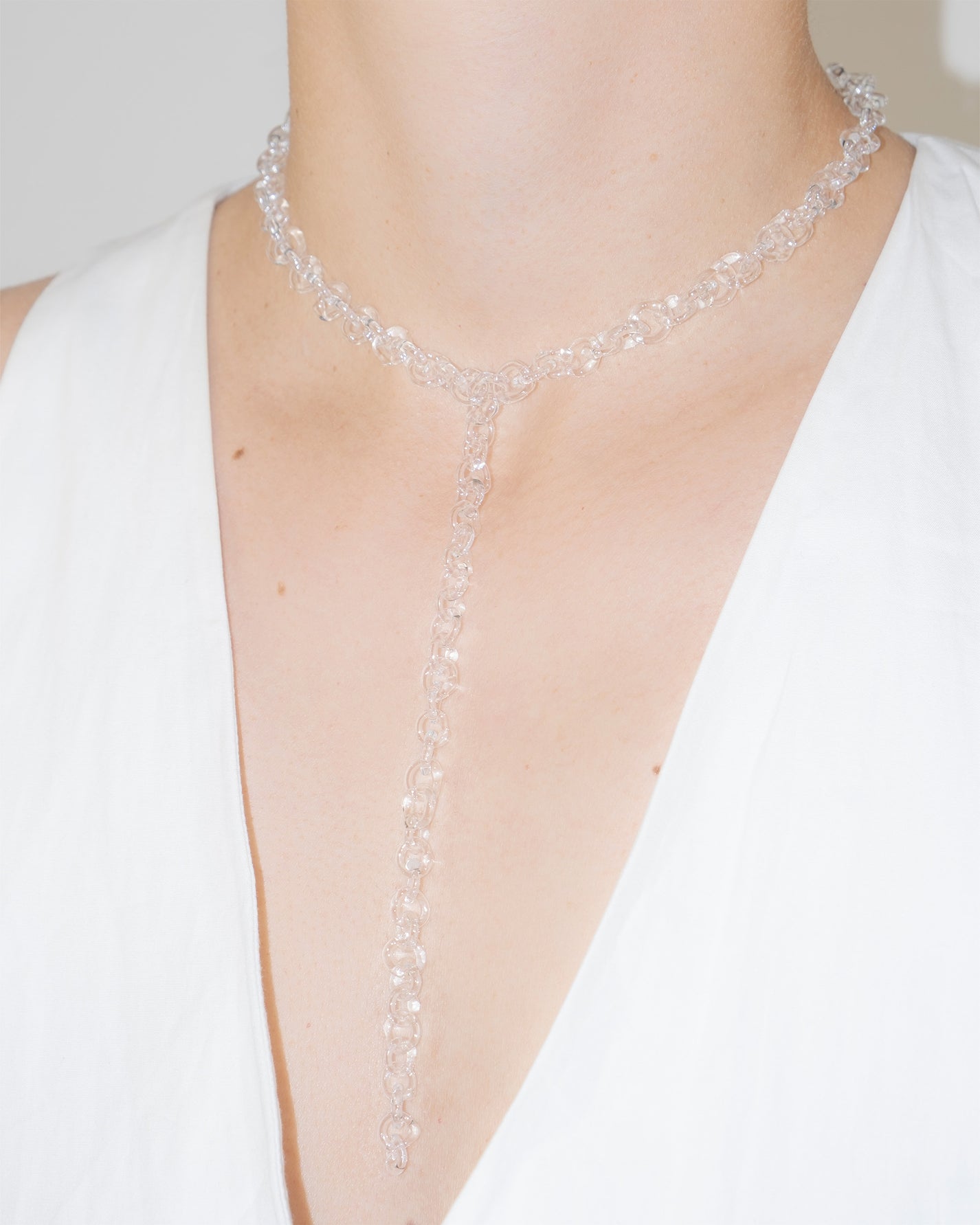 Model wearing thin transparent glass chain necklace with extended drop, styled elegantly.