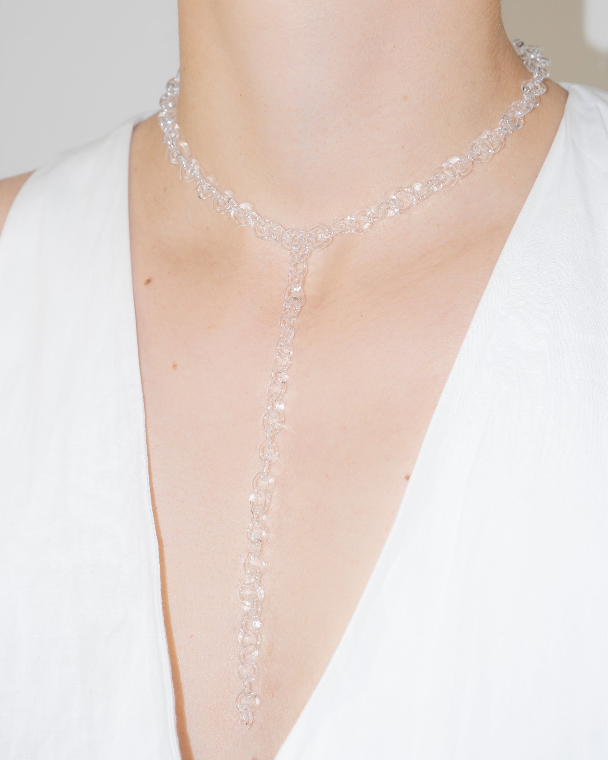 Model wearing thin transparent glass chain necklace with extended drop, styled elegantly.