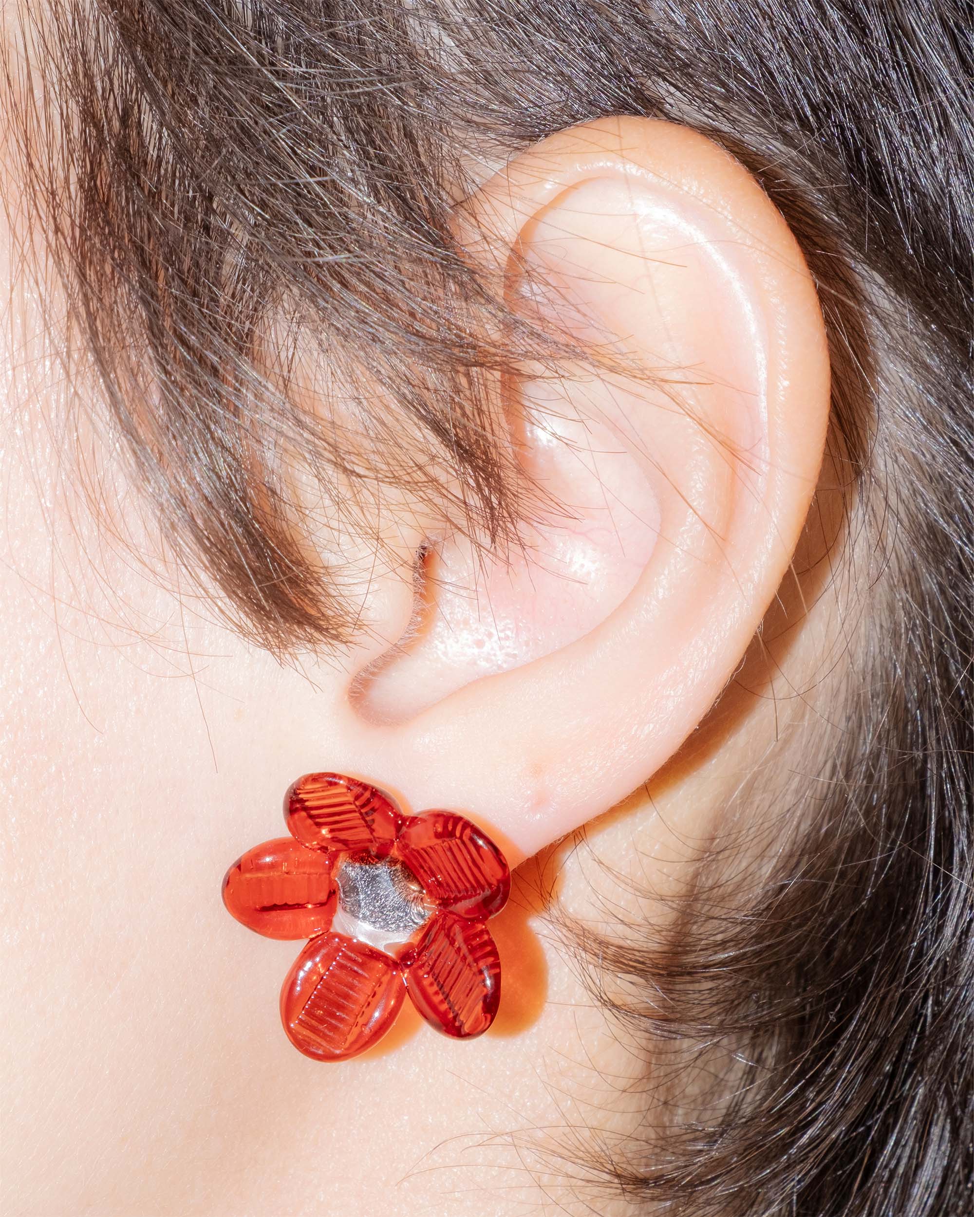 Model wearing Flower Stud Earrings in borosilicate glass with red petals and transparent center, sterling silver studs.