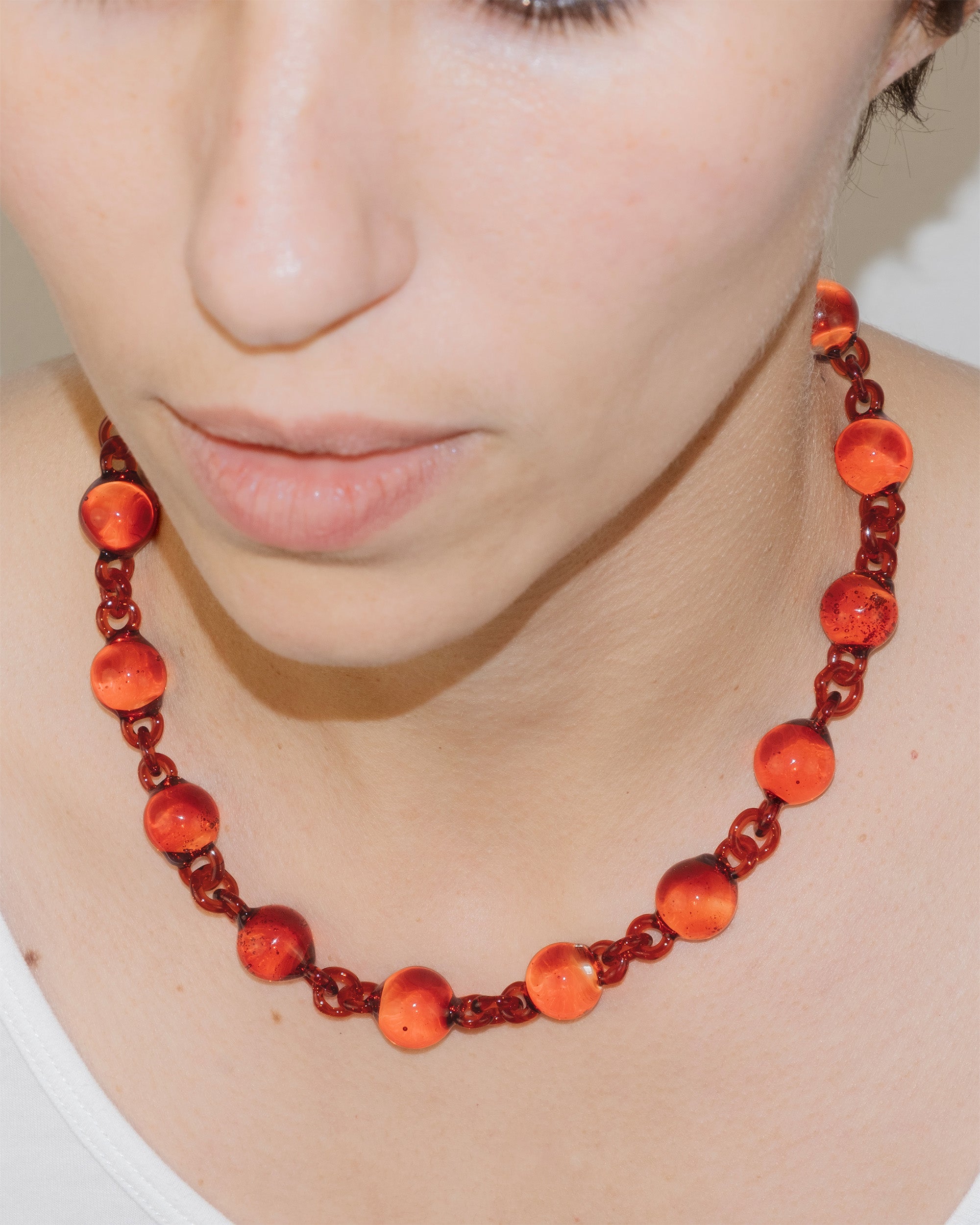 Model wearing red Orb Necklace with solid glass spheres linked into a continuous glass chain, handmade borosilicate jewelry.