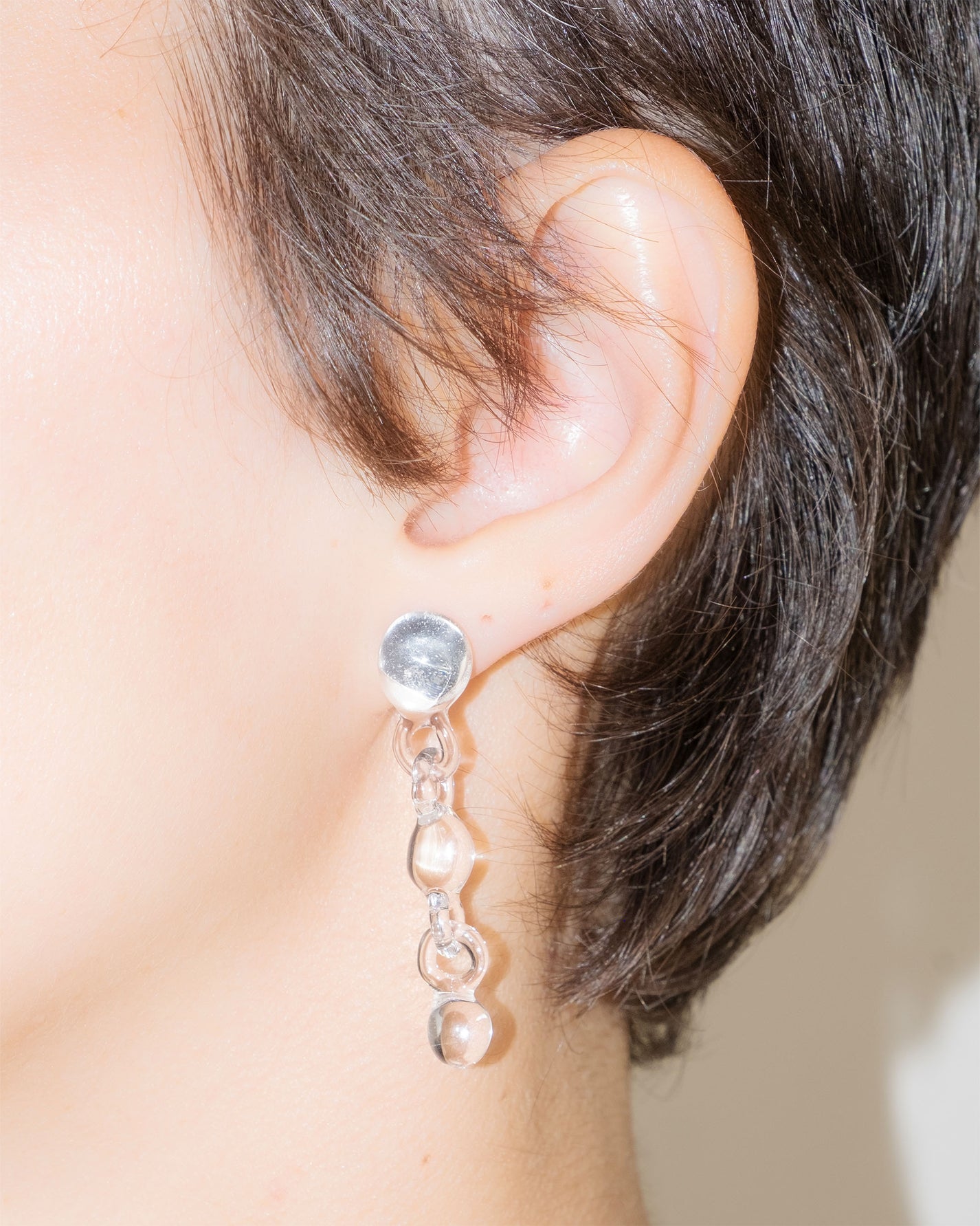 Model wearing Orb Earrings, handmade borosilicate glass design with three orbs in a vertical drop, mounted on sterling silver studs.