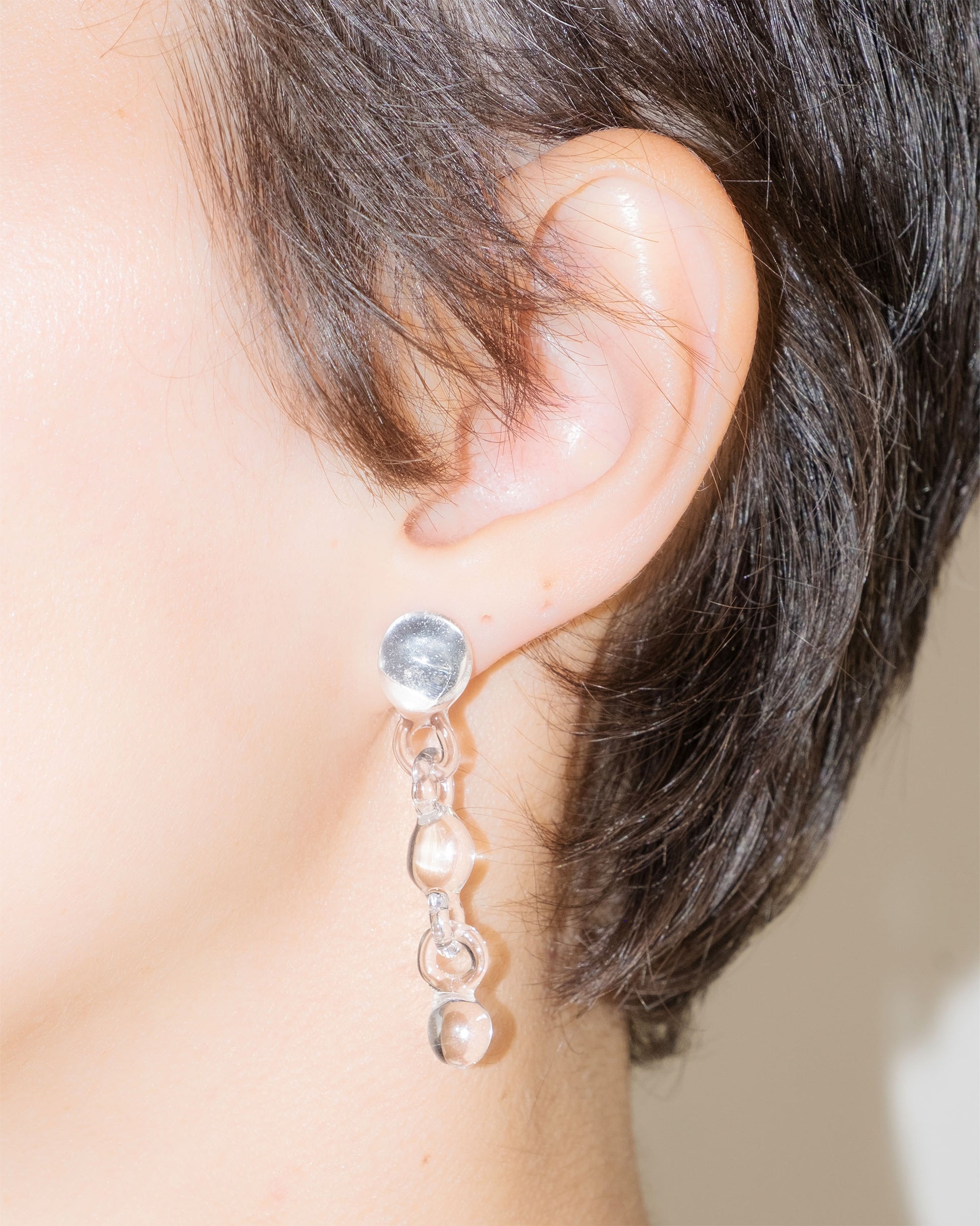 Model wearing Orb Earrings, handmade borosilicate glass design with three orbs in a vertical drop, mounted on sterling silver studs.