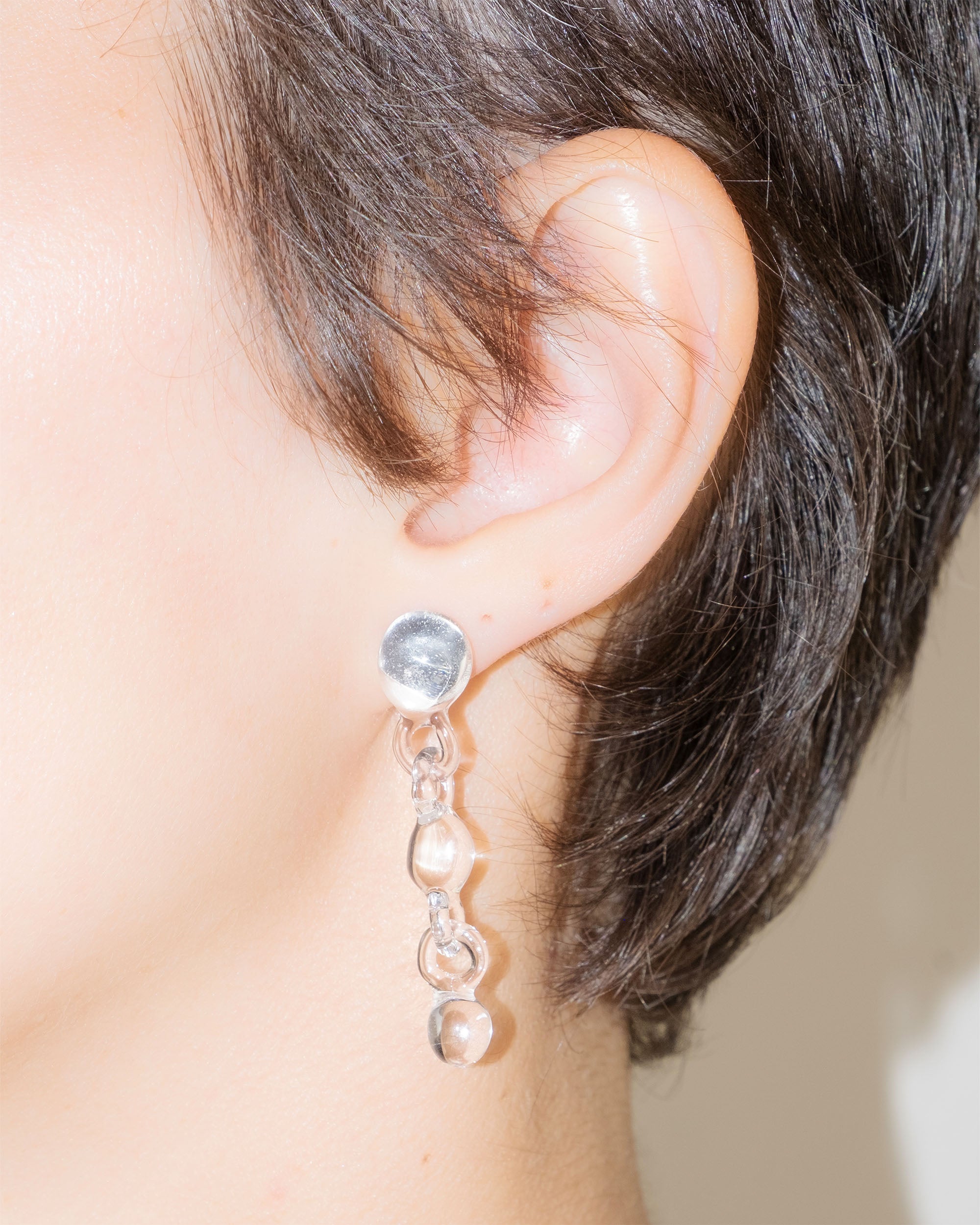 Model wearing Orb Earrings, handmade borosilicate glass design with three orbs in a vertical drop, mounted on sterling silver studs.
