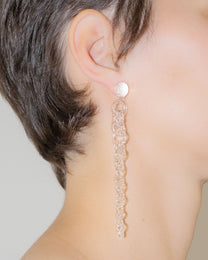 Model wearing Tapered Drop Earrings, handmade borosilicate glass tapering from thick to thin with orb-like top detail and sterling silver studs.