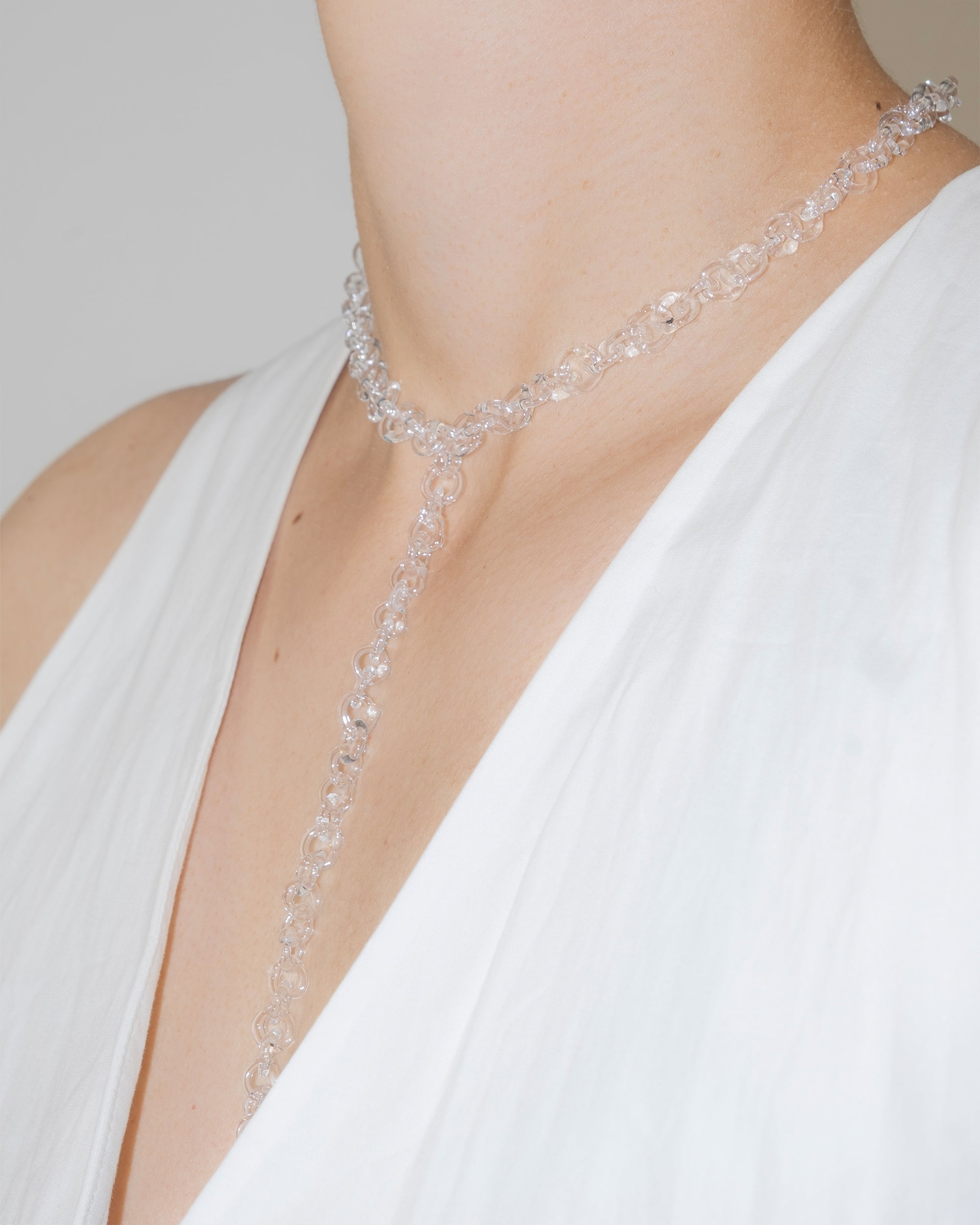 Model wearing thin transparent glass chain necklace with extended drop, styled elegantly, handmade borosilicate links with sterling silver clasp.