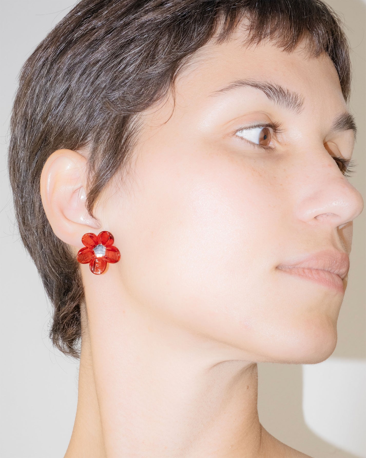 Model wearing Flower Stud Earrings in borosilicate glass with red petals and transparent center, sterling silver studs.