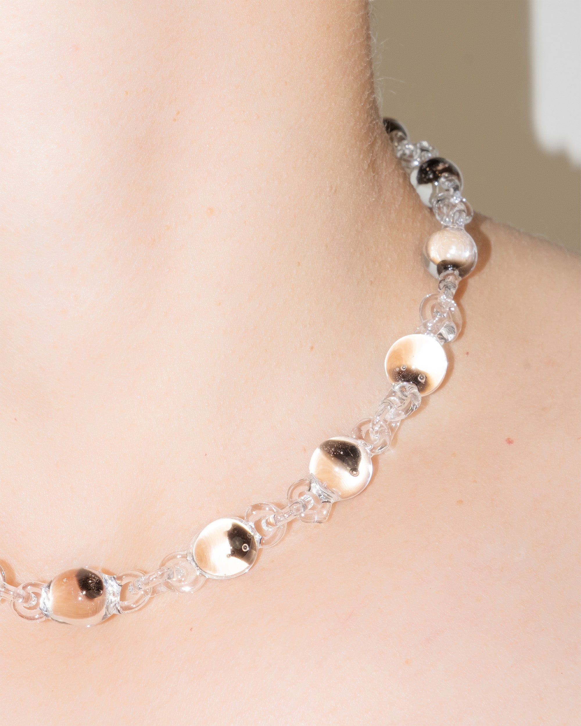 Model wearing Orb Mini Necklace with transparent glass spheres containing black-tinted fading accents, handmade borosilicate jewelry.