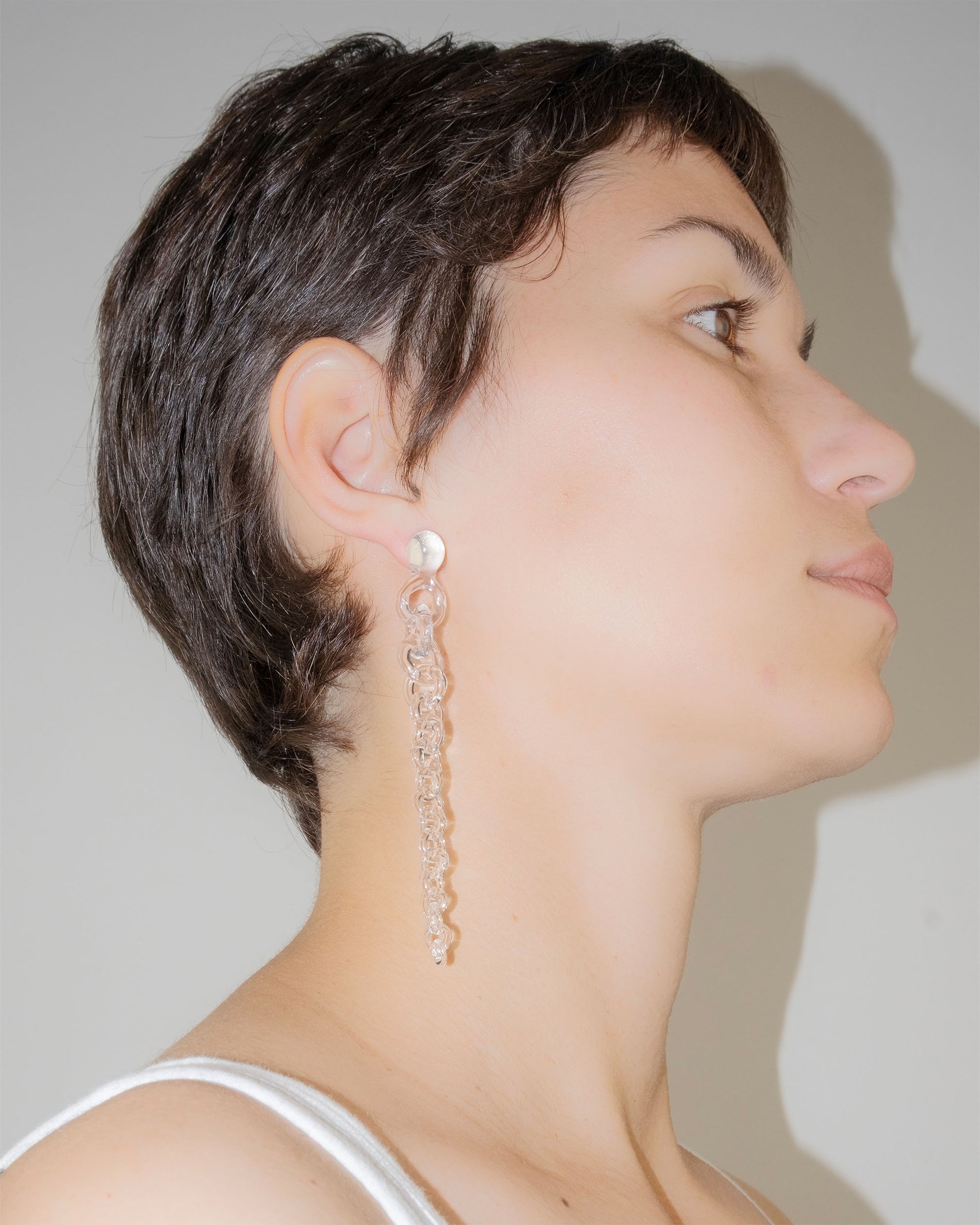 Model wearing Tapered Drop Earrings, handmade borosilicate glass tapering from thick to thin with orb-like top detail and sterling silver studs.