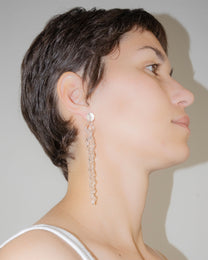 Model wearing Tapered Drop Earrings, handmade borosilicate glass tapering from thick to thin with orb-like top detail and sterling silver studs.