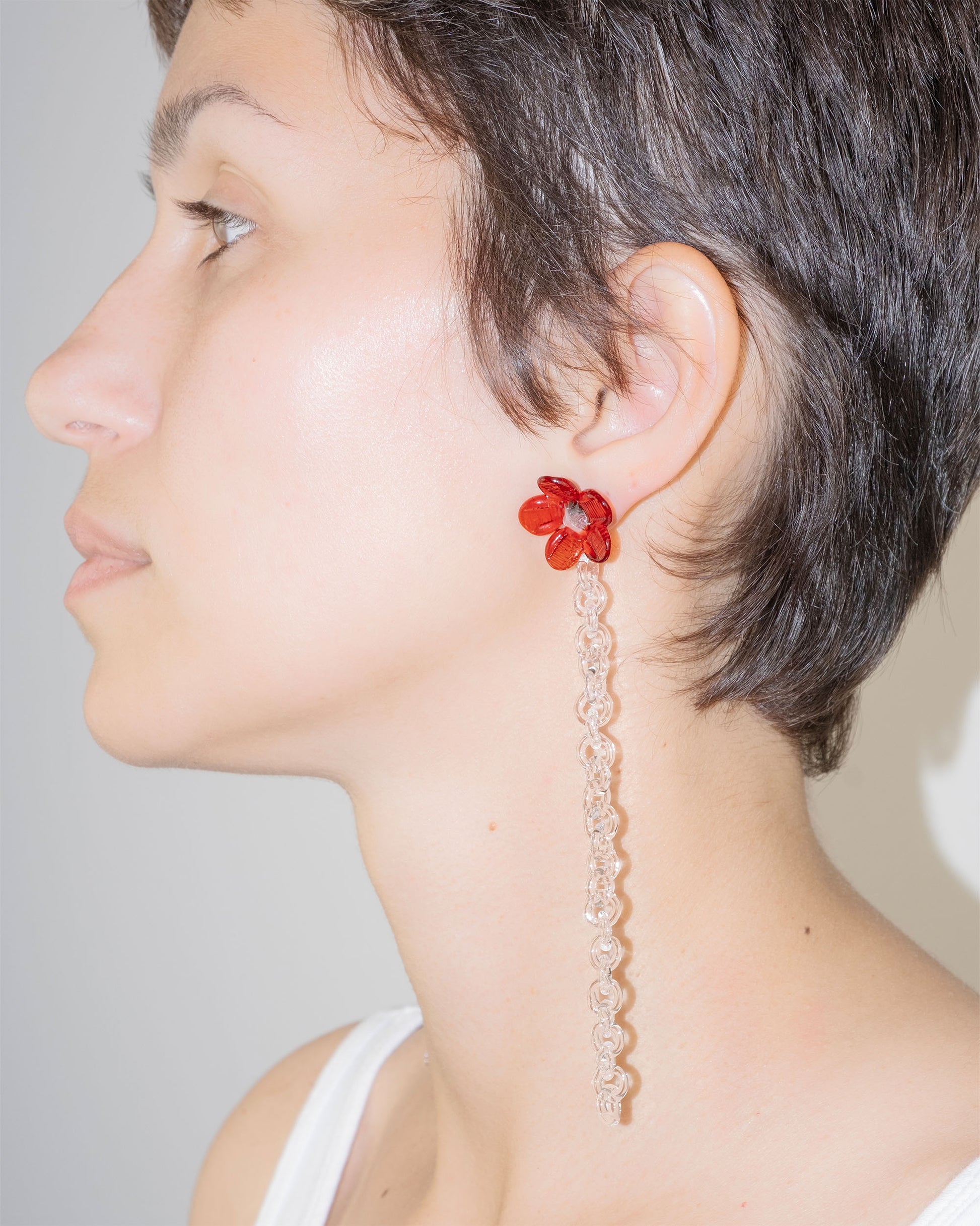 Model wearing Flowered Chain Earrings in red borosilicate glass with transparent center and thin glass chain.