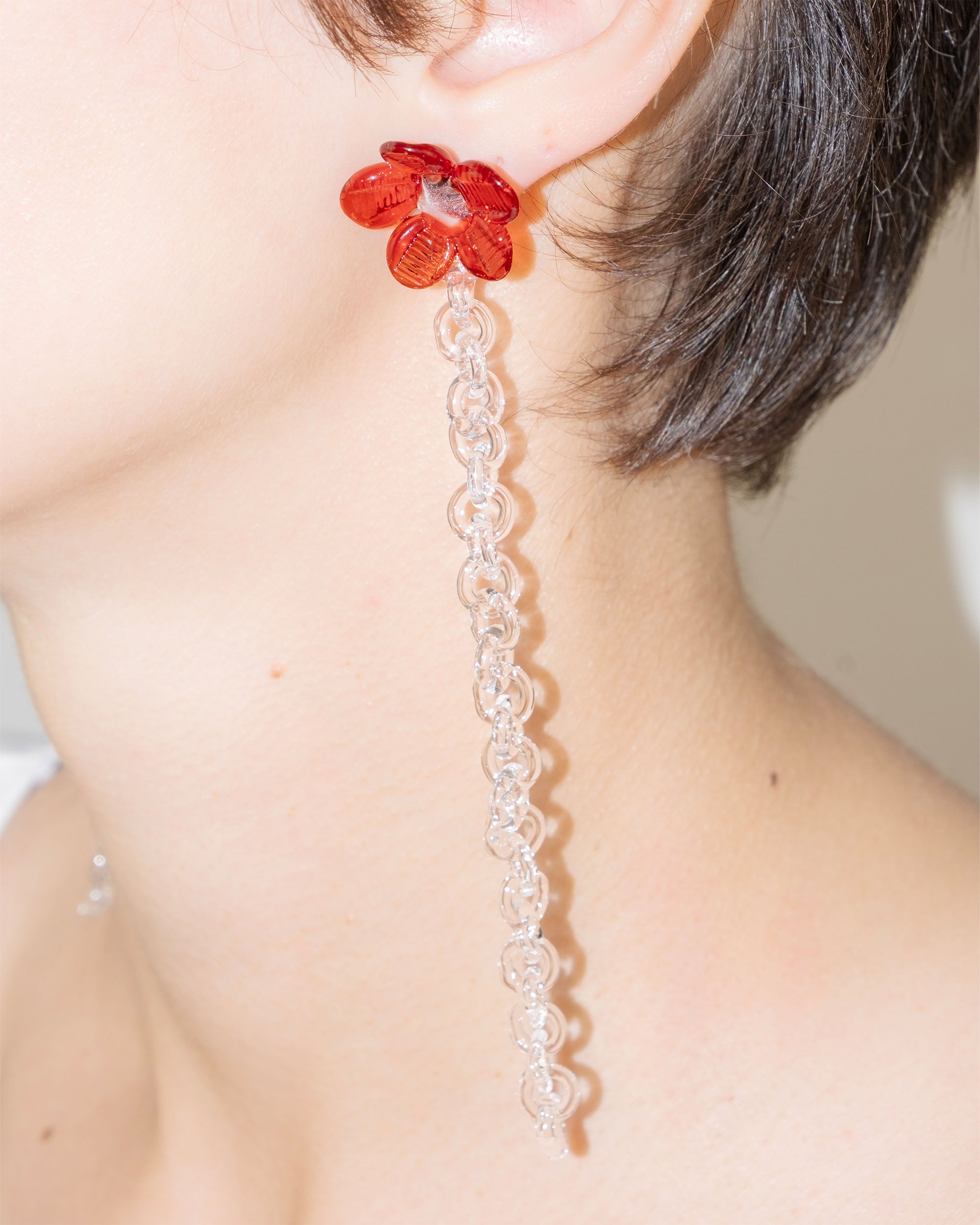 Model wearing Flowered Chain Earrings in red borosilicate glass with transparent center and thin glass chain.