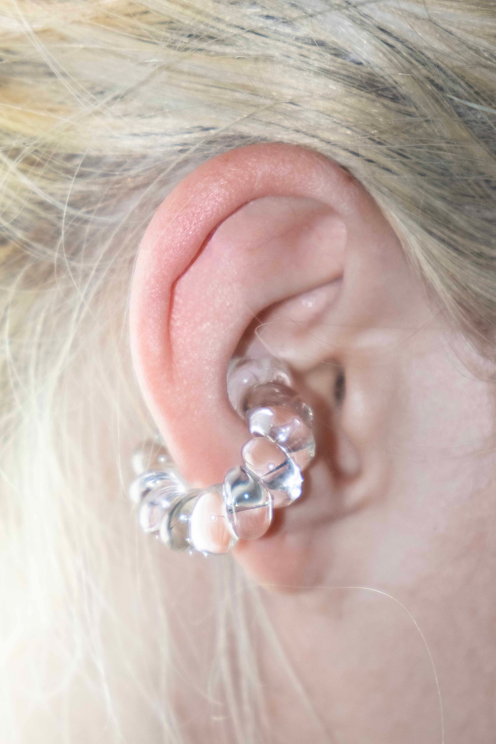 Model wearing a transparent borosilicate glass ear cuff, twisted design, fits without a piercing.
