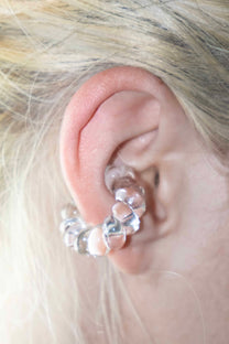 Model wearing a transparent borosilicate glass ear cuff, twisted design, fits without a piercing.